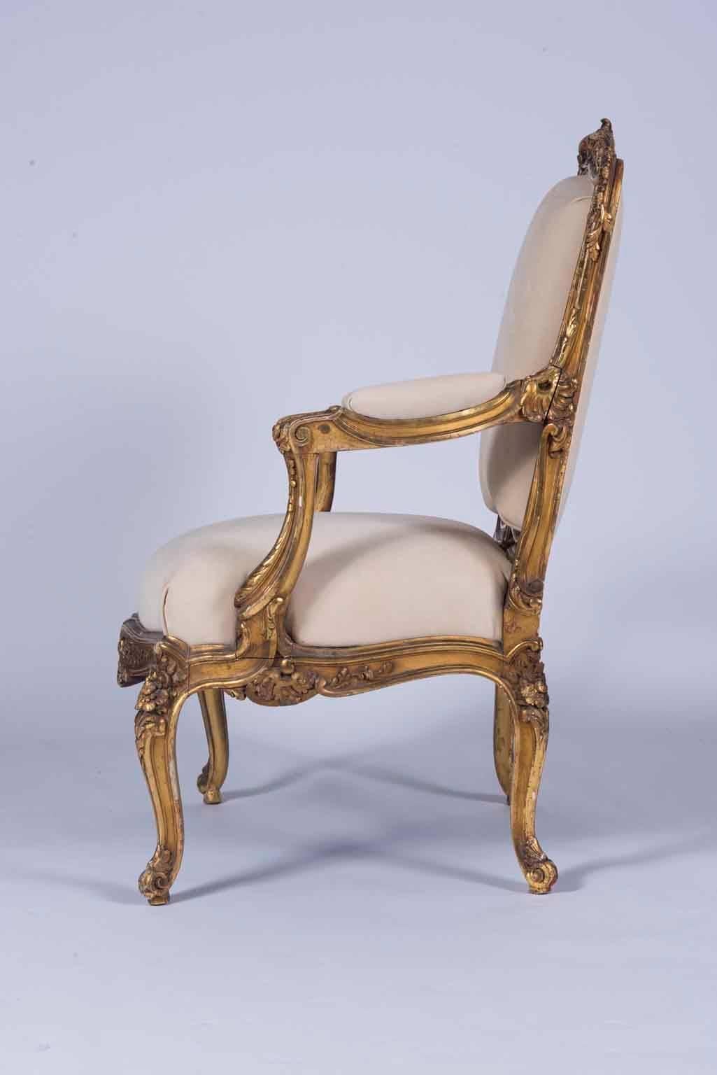 An ornately carved pair of 20th century Louis XV giltwood armchairs newly upholstered in a creamy ecru nubuck Italian leather.