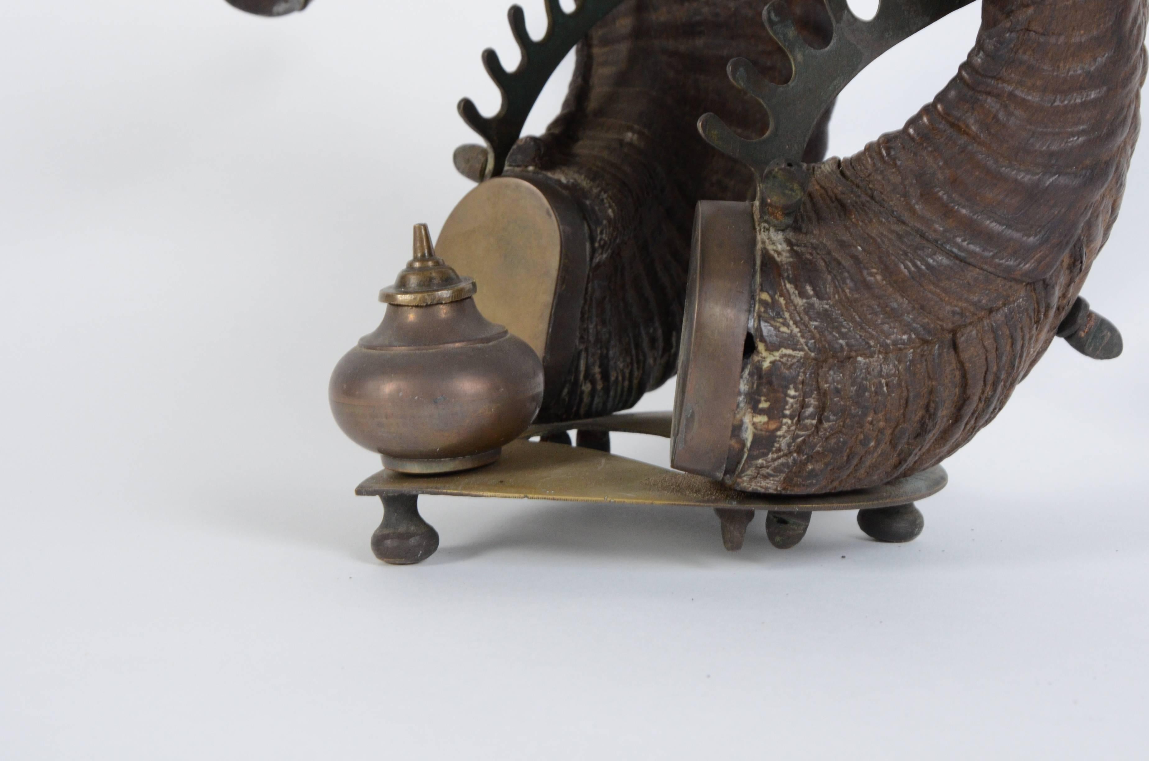 A 19th century Anglo-Indian rams horn inkwell having decorative brass Hindu deities, quill pen supports and ink pot.
