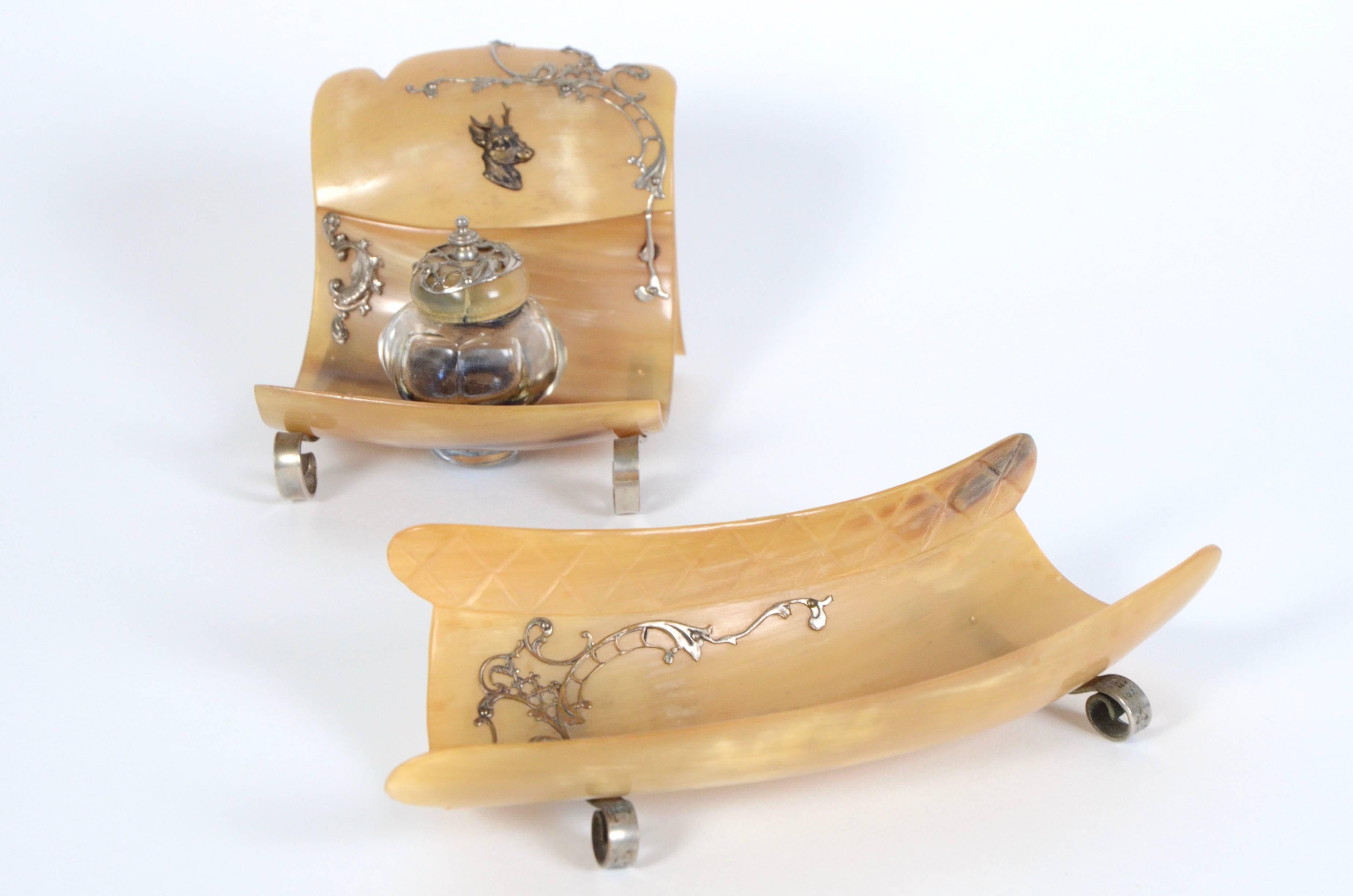 A 19th century continental horn desk set ornately decorated with silver. The small tray is 8 inches long, 3.25 inches deep and 1.75 inches high. The lidded glass inkwell is 4 inches wide, 5 inches deep and 3.25 inches high.