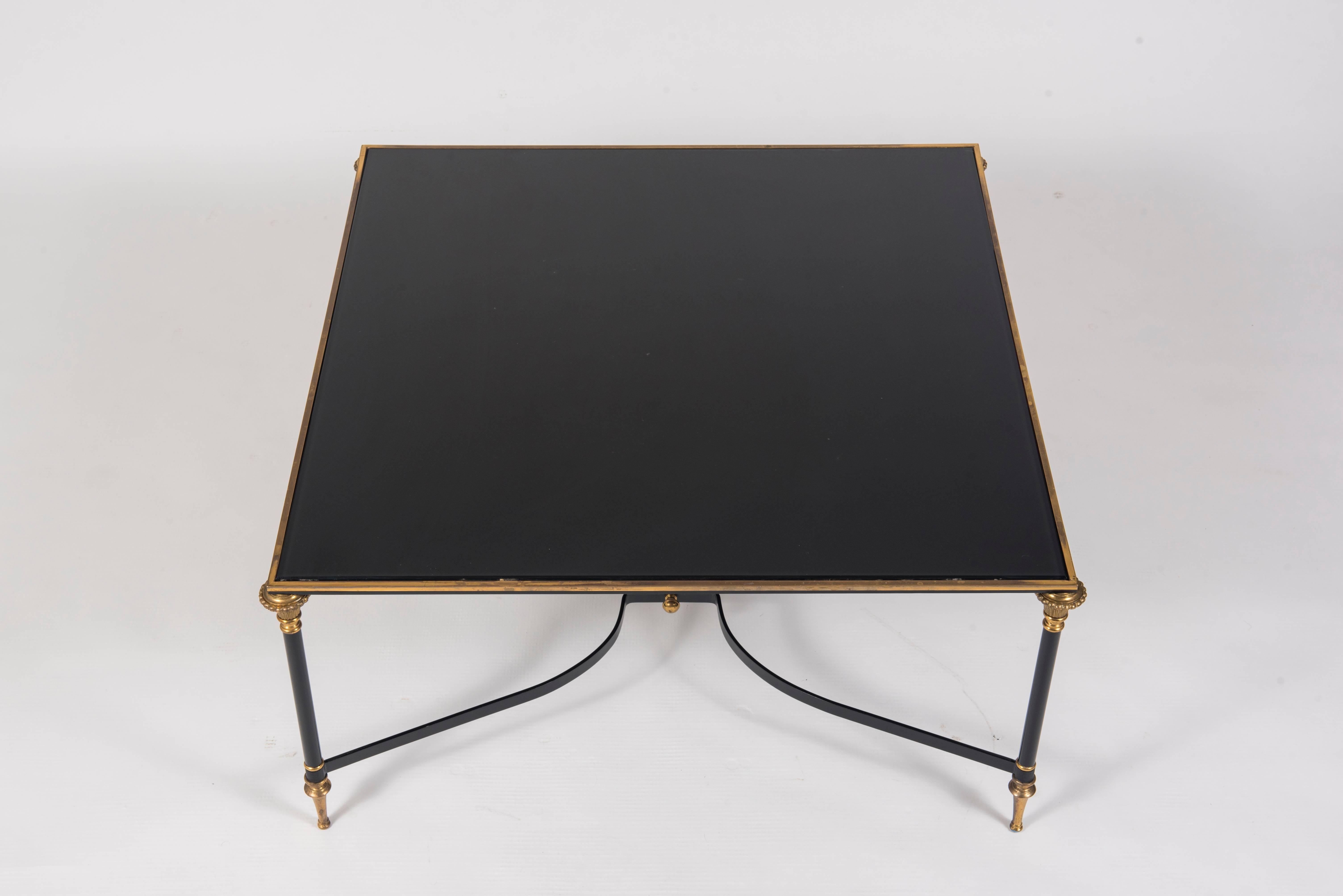 A chic 1960s black enameled steel and brass Maison Jansen style cocktail table. This table features a new piece of solid black eglomisé glass.