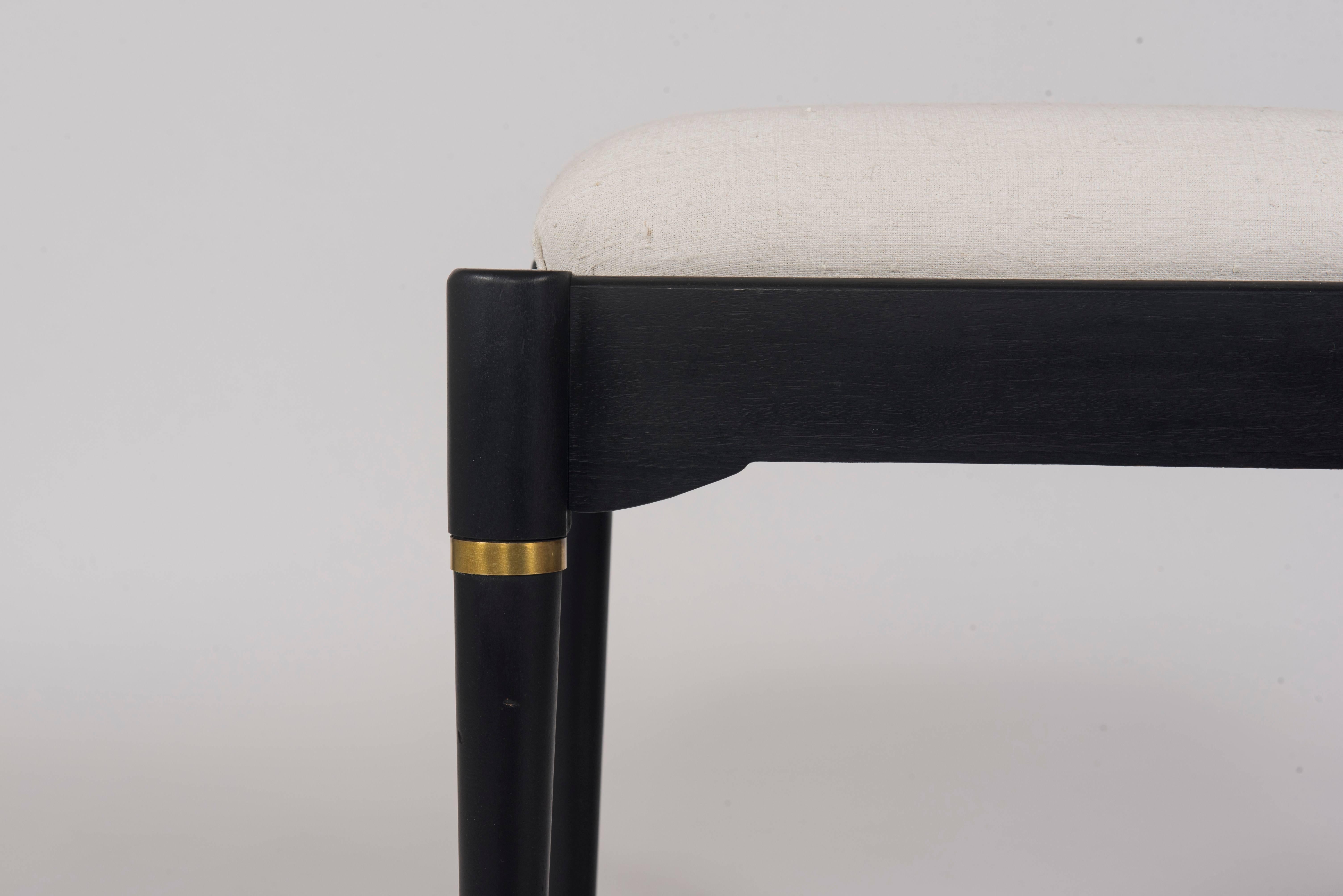 A sturdy ebonized wood ottoman with brass banding and sabots newly upholstered in a ecru linen.