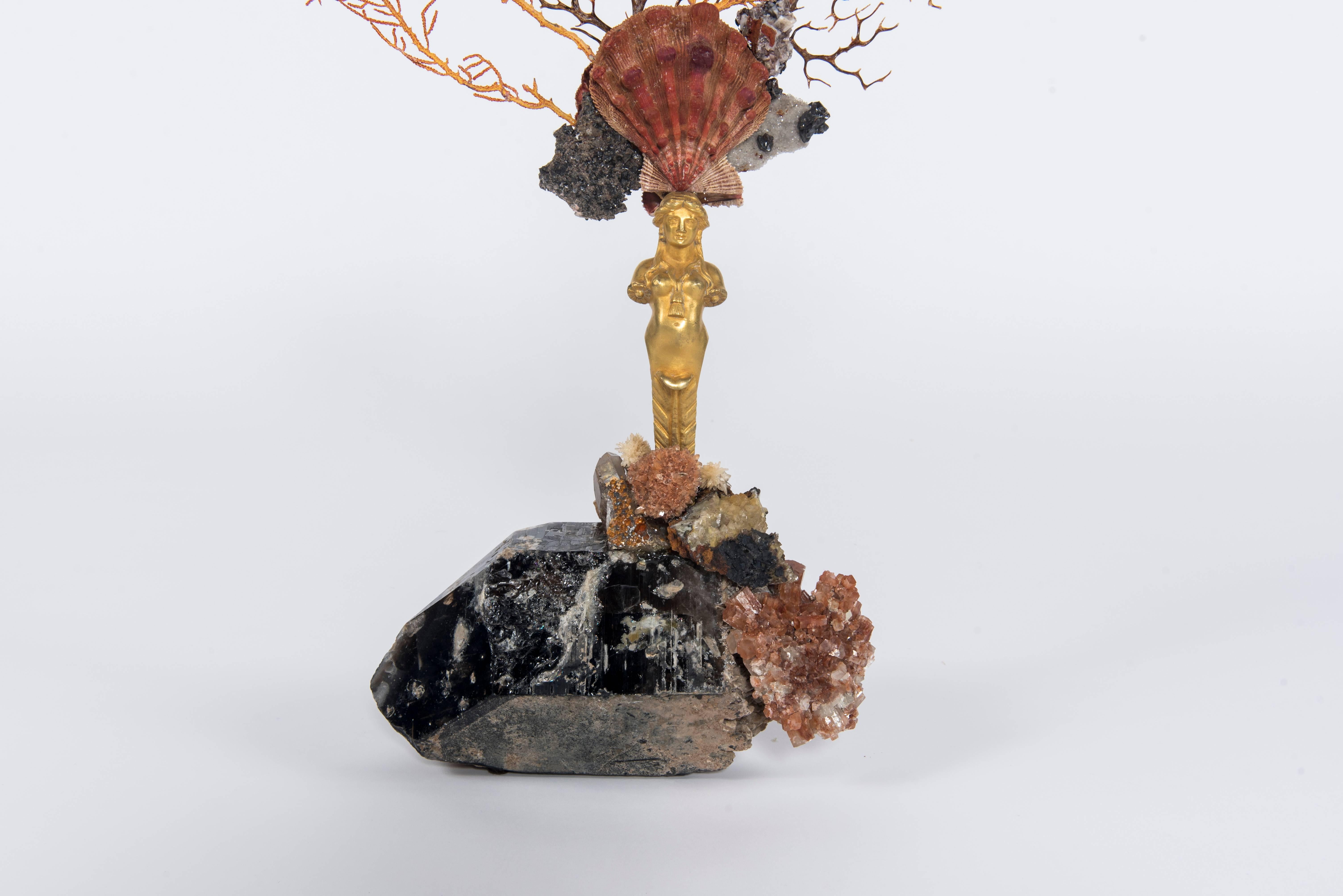 Calypso I sculpture. An early 19th century bronze doré caryatid sits atop a large natural smoky quartz base. Her head is beautifully affixed with a crown adorned by a rare complete lion's paw shell, mixed sea fan corals and minerals. The bounty of