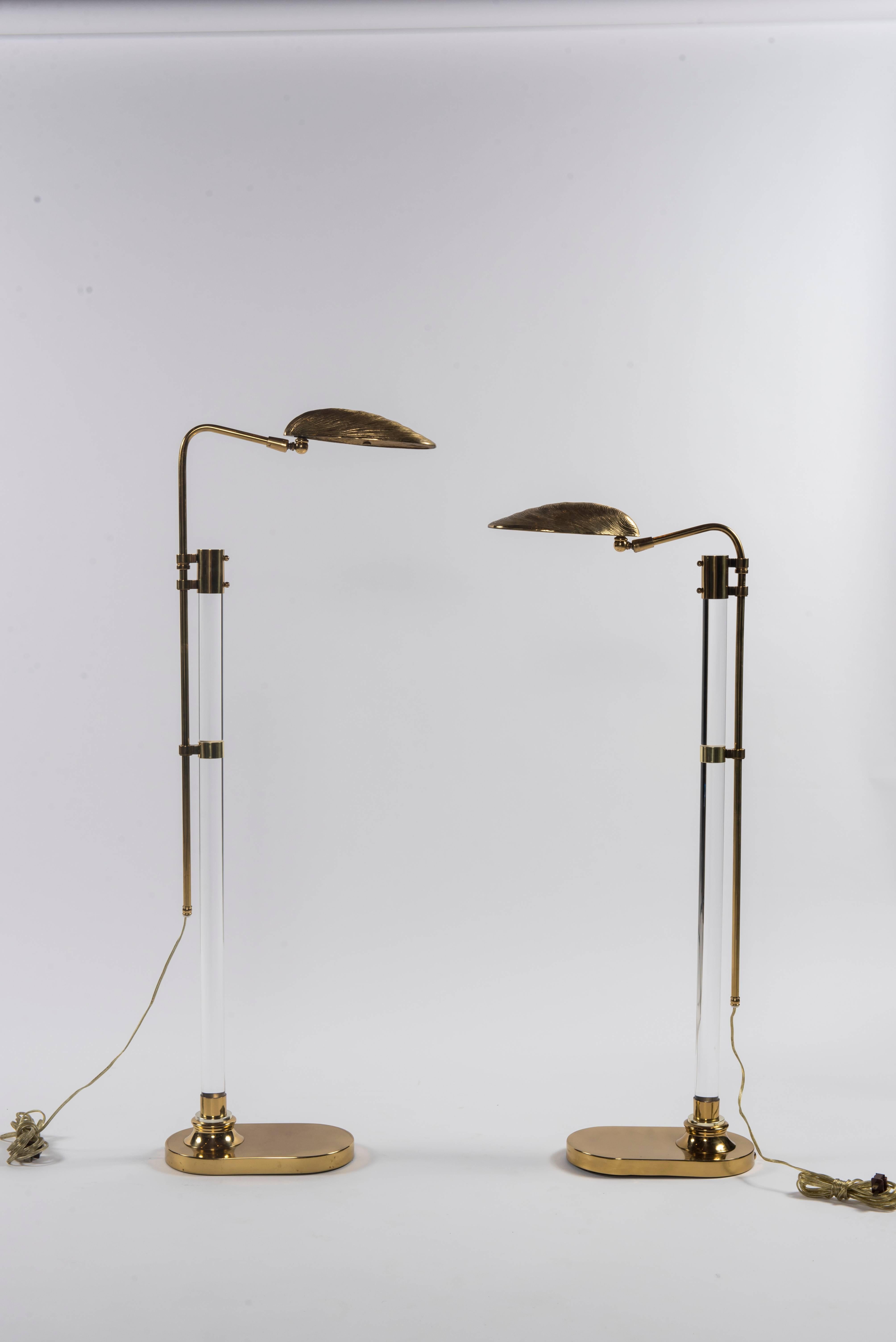 A chic pair of lucite and brass clam shell floor lamps. The lamp heads pivot and the height is adjustable.