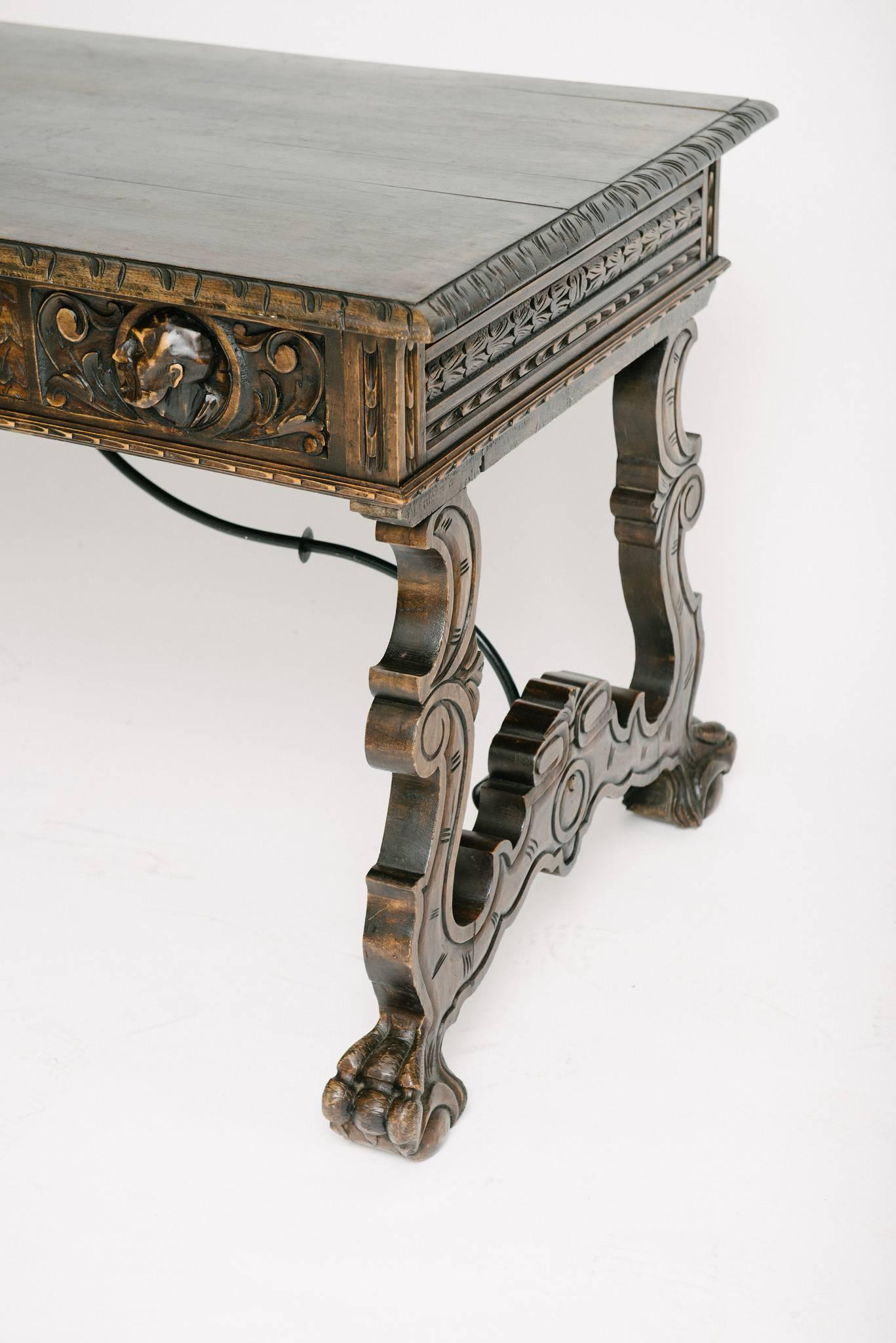 An ornately carved Renaissance style desk with three drawers and iron stretcher.