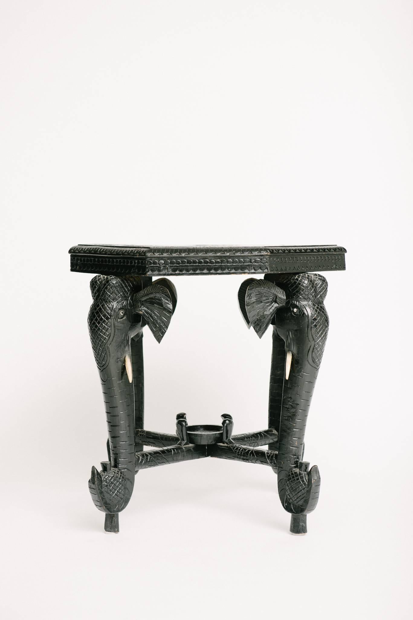 An ebonized and carved occasional table with four elephant heads and octagon top.
