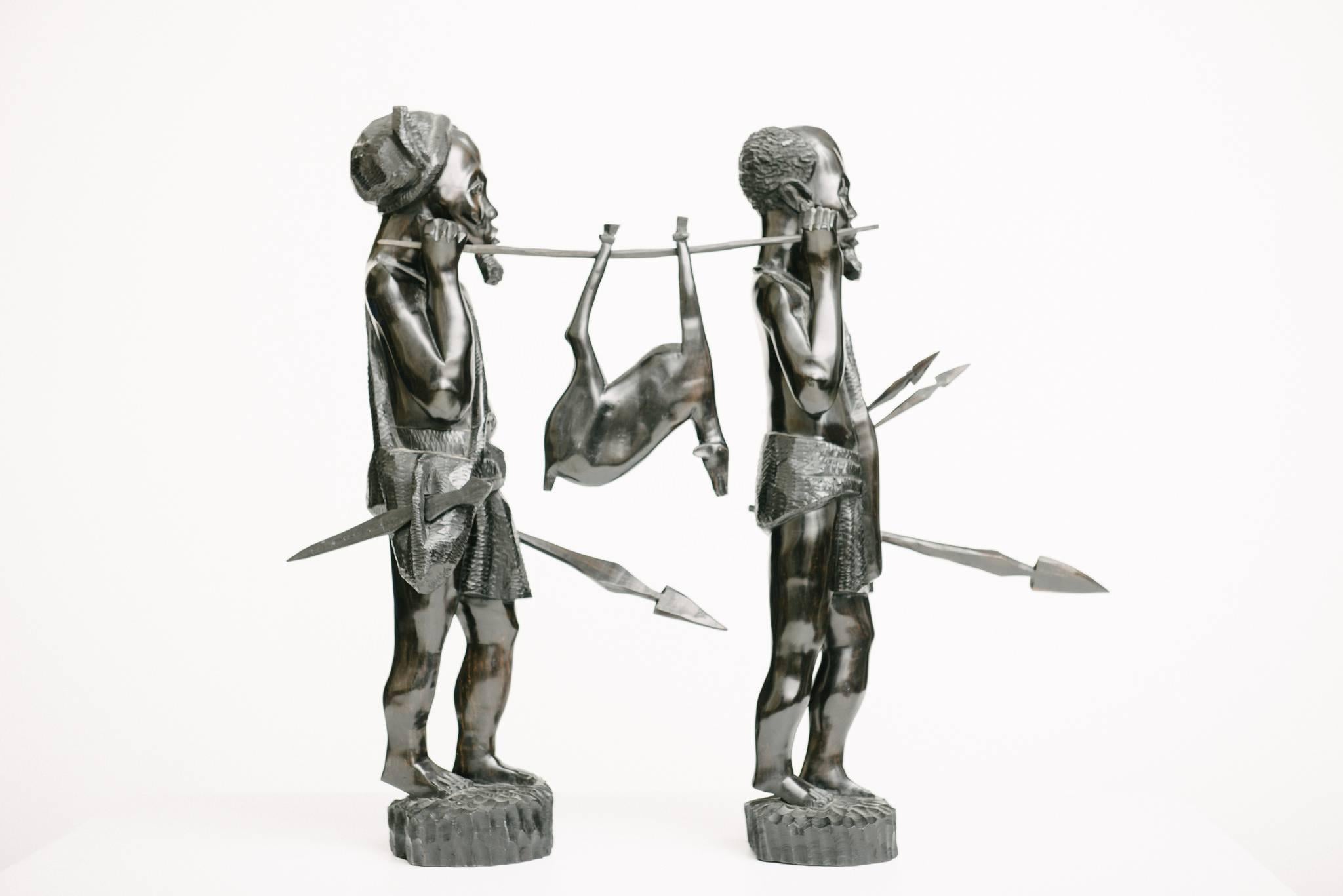 Pair of early 20th century African ebonized carved wood hunters with kill and hunting tools.