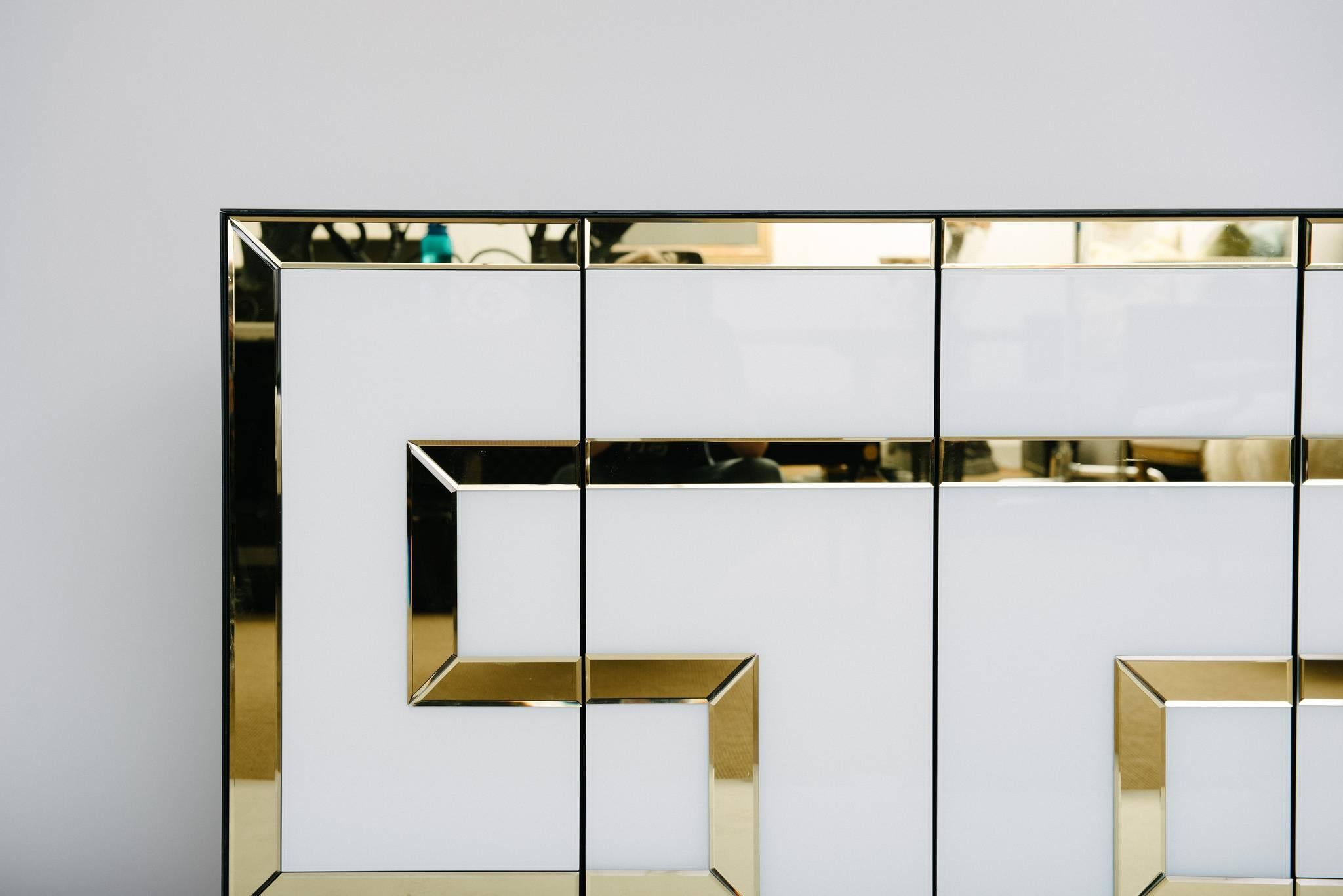 A chic and glamorous 1970s Italian credenza. This cabinet features black and white glass and is accented with a large gold beveled mirror Greek key detail.