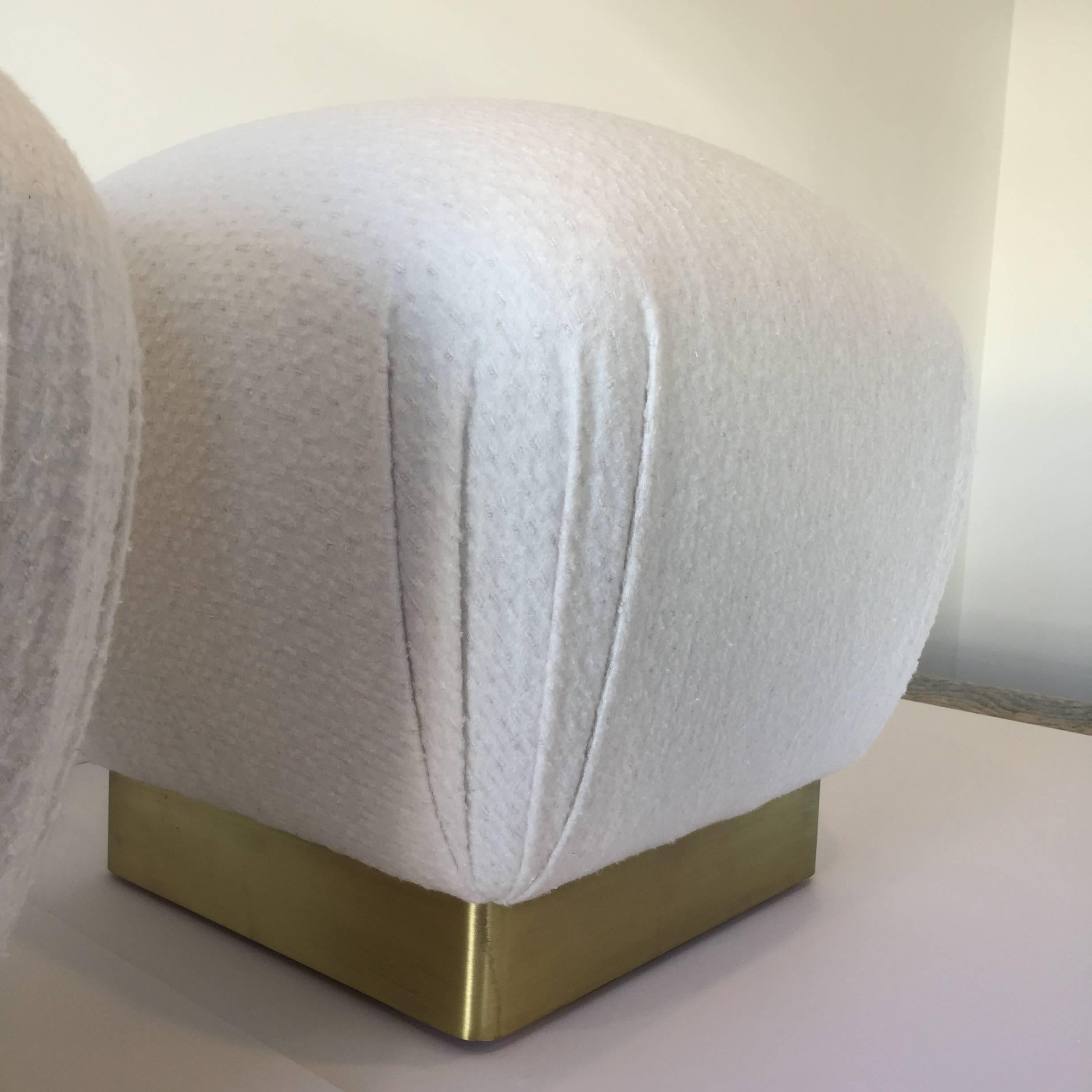 A custom pair of Karl Springer Style Souffle pouf ottomans upholstered in a Sunbrella ivory bouclé fabric with brass bases.
