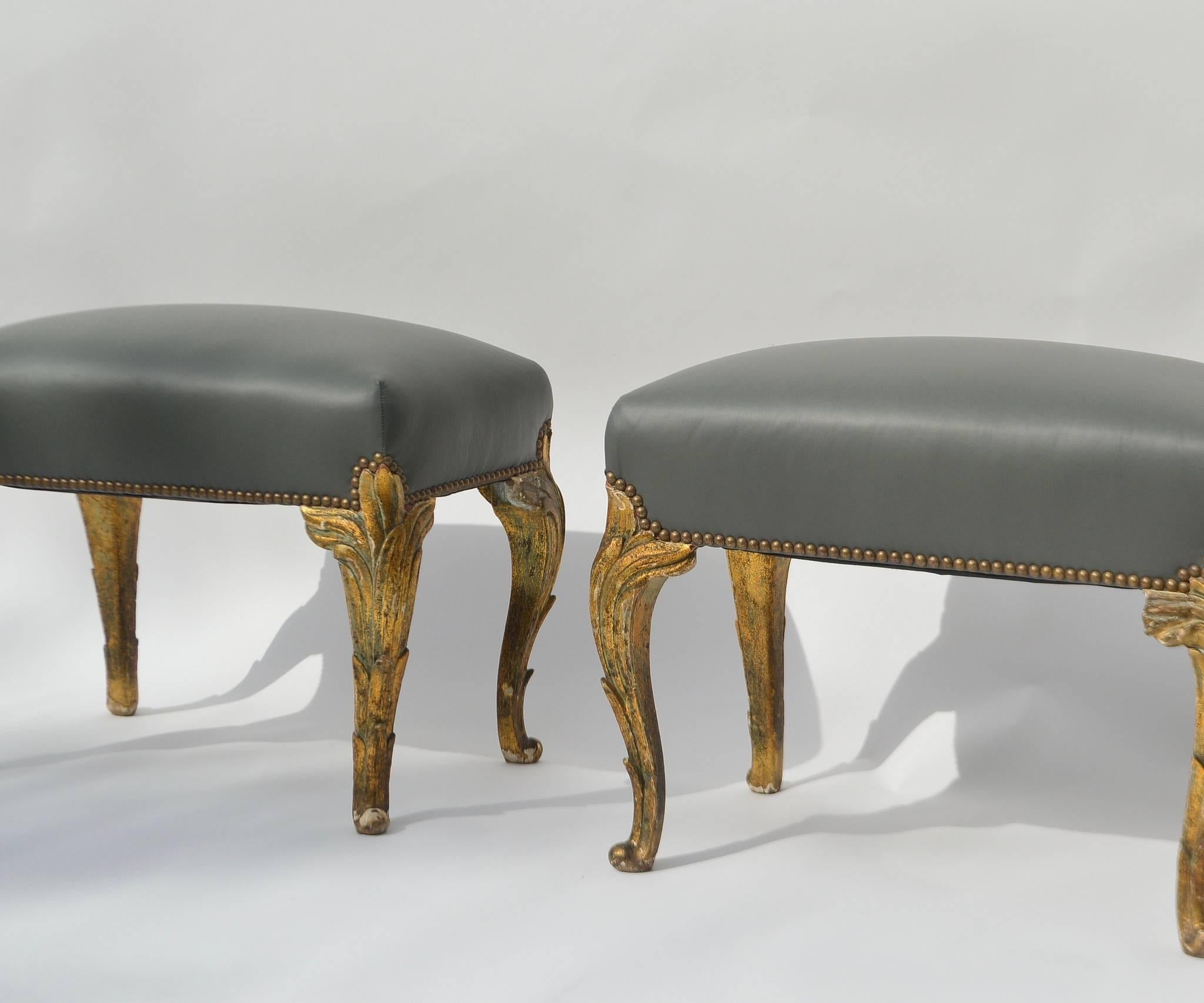 A pair of French Art Nouveau carved gilt wood ottomans newly upholstered in grey leather with nailhead detail.