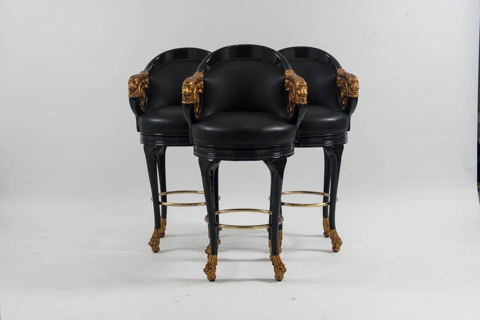 A set of three newly black lacquered and gilt wood Empire style leather barstools. Each of these newly upholstered barstools feature French nailhead detailing, a brass footrest, and swivel.