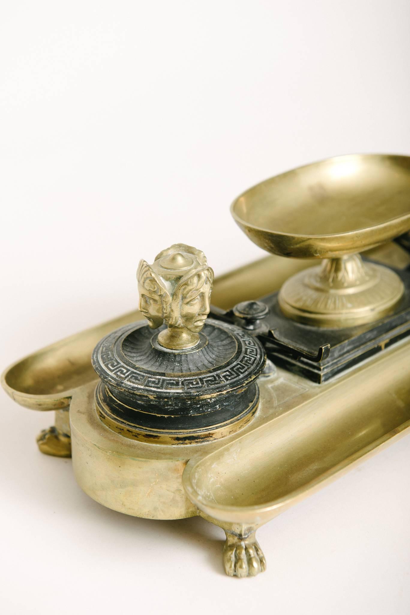 A 19th century neoclassical bronze desk set featuring two inkwells that are flanked by two elongated trays with a centre oval pedestal dish. The inkwells are black patinated sporting a Greek key motif and are topped with a three face decorative