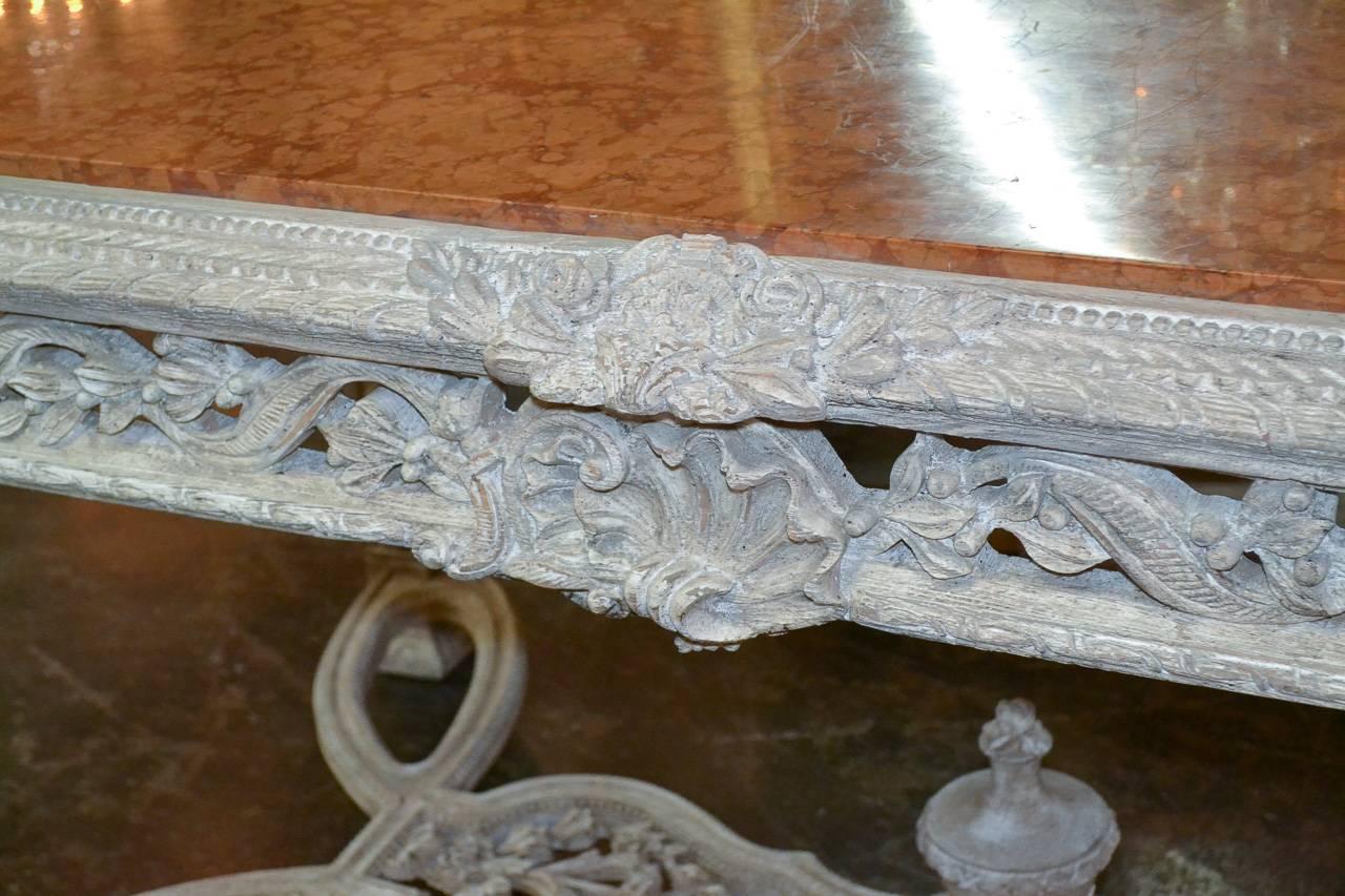 Gorgeous French hand-carved center table with painted finish and Rouge de Verone marble top. Having ornately carved apron in acanthus leaf, ribbon and laurel motif. Resting on beautiful tapered legs and tied together with elaborate stretcher with