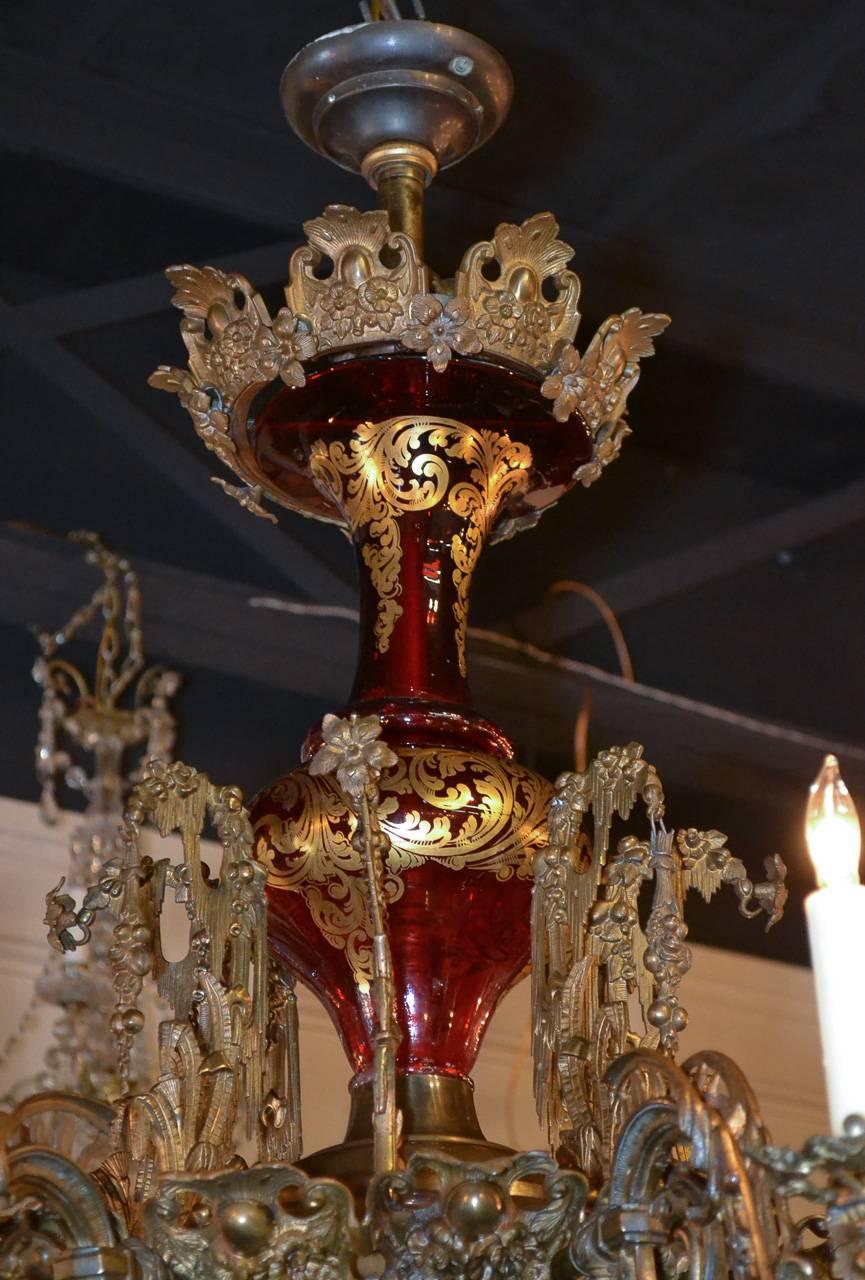 Marvellous eight-light 19th century Belle Époque bronze and glass chandelier, circa 1880. Having beautiful deep red glass central column with gold overlay, detailed cast bronze frame adorned with acanthus leaf motif and arms terminating in gryphons