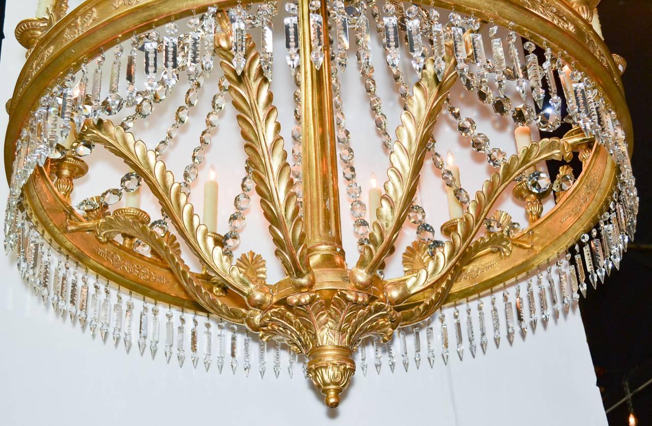 Sensational 19th century Italian giltwood and crystal sixteen-light chandelier. Having lustrous giltwood frame in carved acanthus leaf motif, adorned with ring a of cut crystal prisms, and detailed in bird and classical designs around frame. 