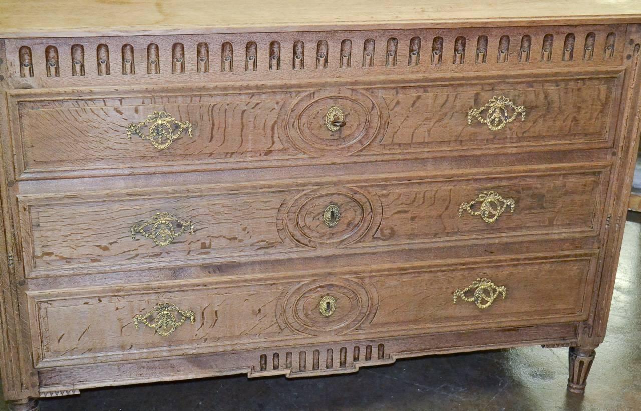 Marvelous 18th century French Louis XVI bleached oak three-drawer commode. Having carved drawer fronts and fluting, beautiful bleached finish, tapered feet and interesting gilt bronze hardware in ribbon, wreath and swag motif. 