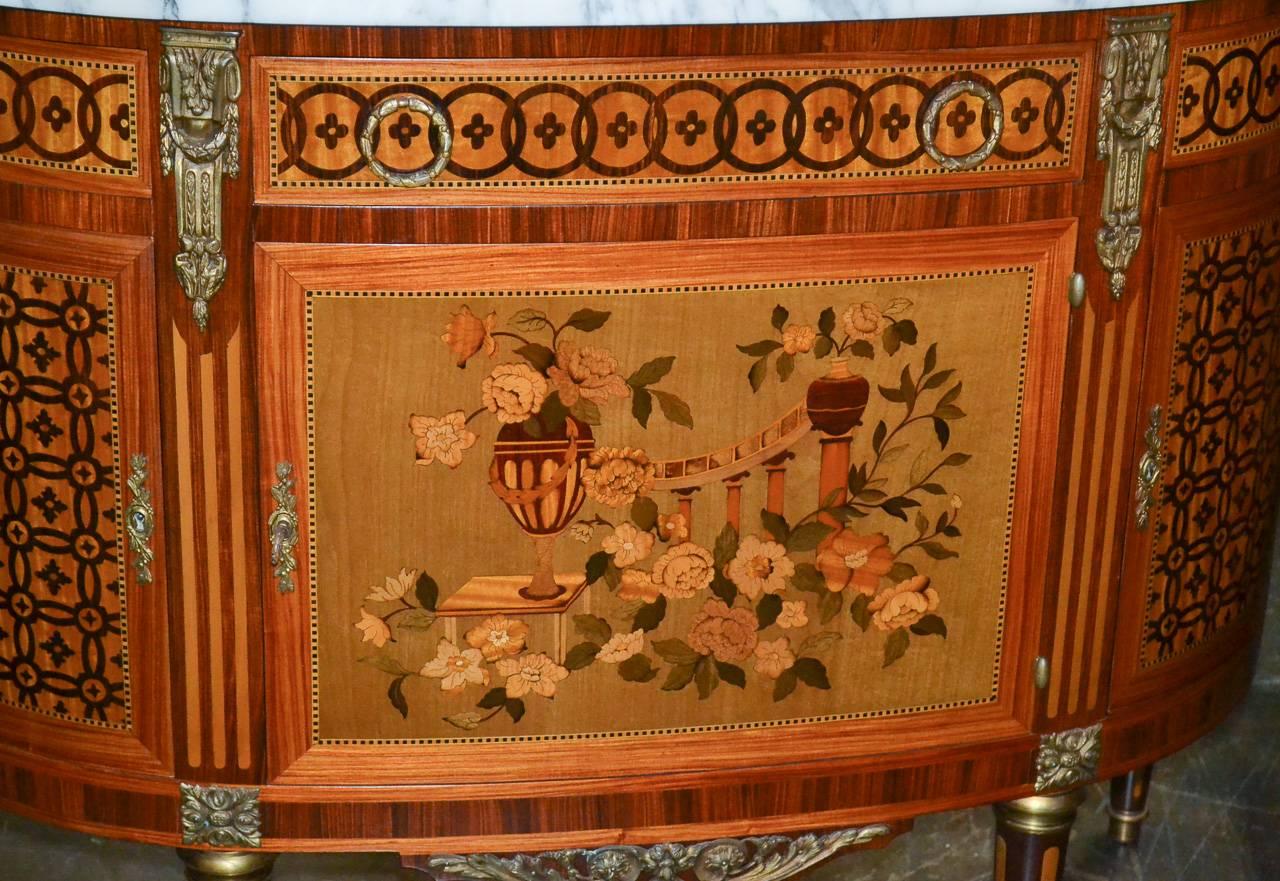 Marvelous Italian demilune server with marquetry inlays and Carrara marble top. Having three drawers over three doors, bronze mounts and hardware in classical motifs, and lovely inlaid marquetry design of floral setting. 