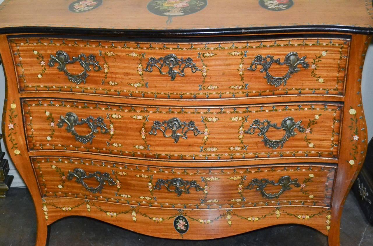 Wonderful eclectic 19th century English hand-painted satinwood three-drawer commode. Having beautiful later painted floral designs on all sides, intricate bronze hardware, and lovely warm rich patina. 