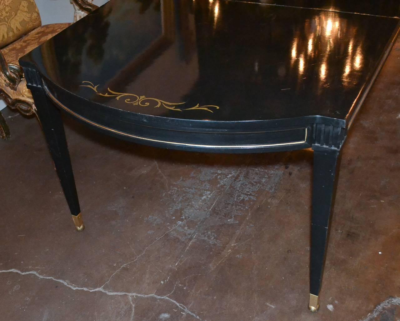 Versatile French neoclassical black lacquered dining table. Having parcel-gilt detailing and trim, foliate inlays on top, shaped ends, and resting on tapered legs. Exhibiting a beautiful patina and clean lines that work in countless styles of decor!