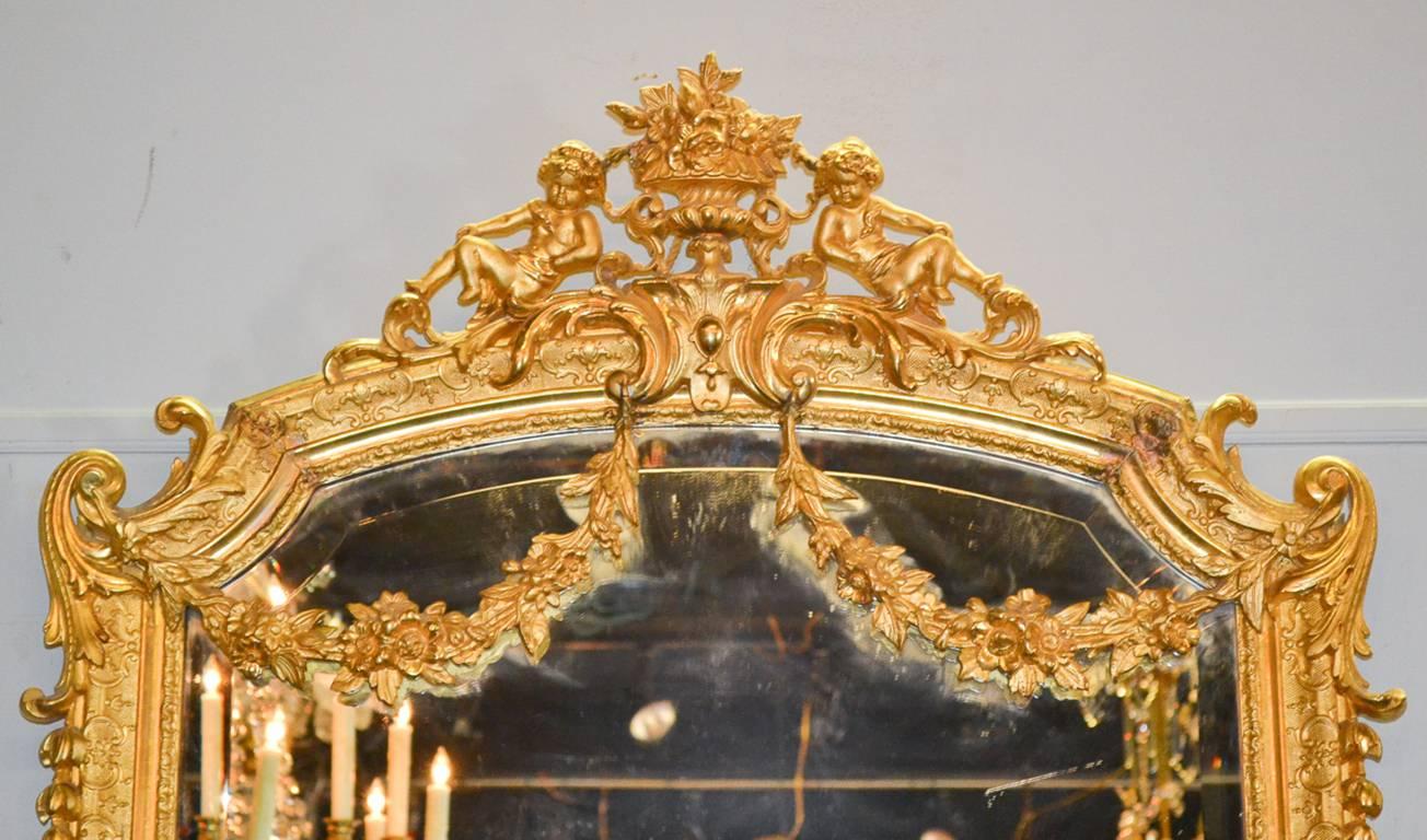 Sensational pair of French Louis XV style water gilded mirrors. Having a beautifully carved cartouche with reclining putti and floral urn, beveled mirrored glass and detailed carved frames with acanthus leaf and floral swag adornments. Exhibiting a