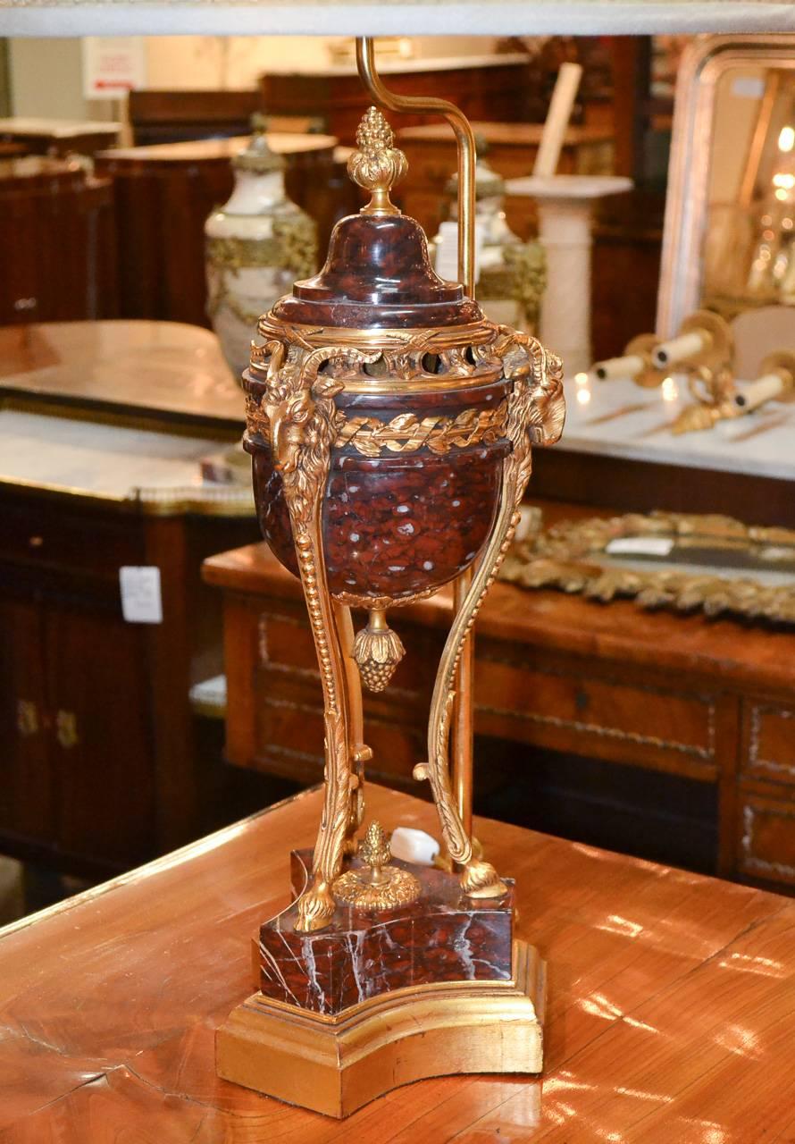 Superb pair of 19th century French urns mounted as lamps. Having lovely Griotte rouge marble, bronze frame with ram's head and cloven foot motif, and lustrous gilt bronze finish. An elegant piece with Classic lines to suit a variety of decorative