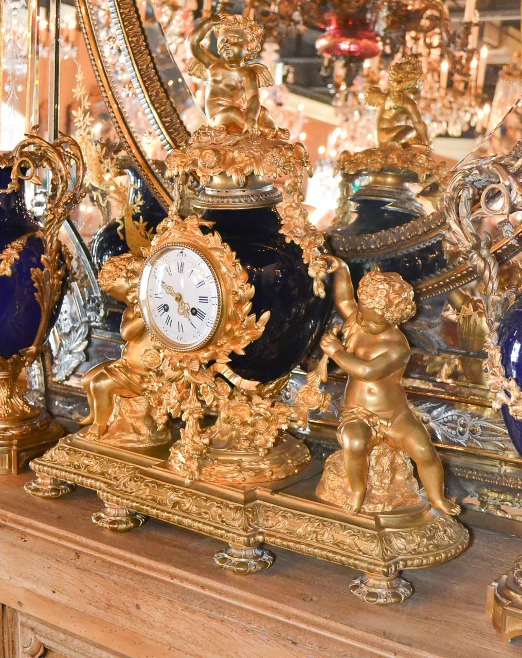 Exceptional 19th century French doré bronze and cobalt three-piece garniture. Having finely cast gilt bronze putti surrounding central clock, elegant draped bronze swag, and lovely cobalt urns. A stunning piece for numerous designs! 
 Clock