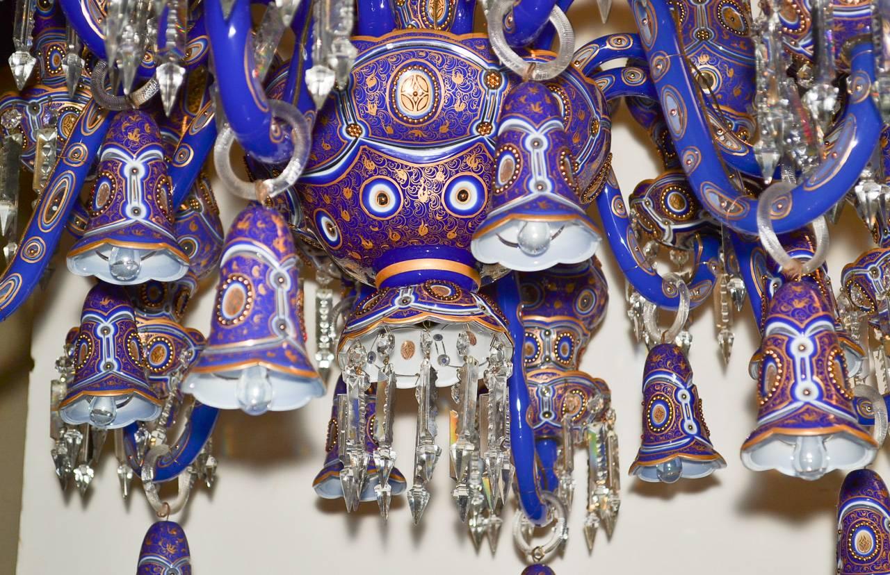 Spectacular pair of Austrian painted and enameled blue glass twelve-light chandeliers. Having impressively detailed hurricane shades, gracefully curved arms, and accented with oil drop crystal prisms and bell shades. Wonderful for numerous designs!