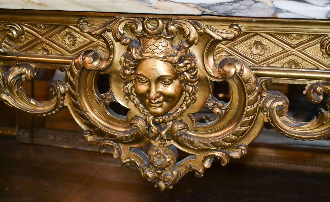 Exceptional 19th century, French Regency carved giltwood console. Having beautifully carved frieze with mask of lady and acanthus leaf motif, detailed X-stretcher, lustrous gilt finish, and impressive Escalates alpha marble top. A very sophisticated