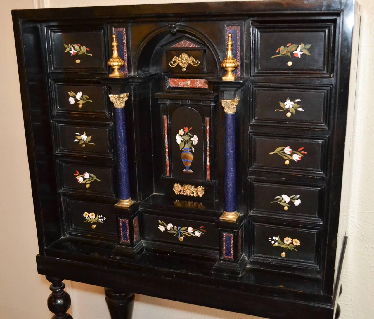 Marvelous 19th century Continental pietra dura inlaid bargueno, circa 1880. Having colorful pietra dura inlays across fitted drawers in floral motif, lovely aged black lacquered finish, and resting on later Spanish base (circa 1980). A splendid