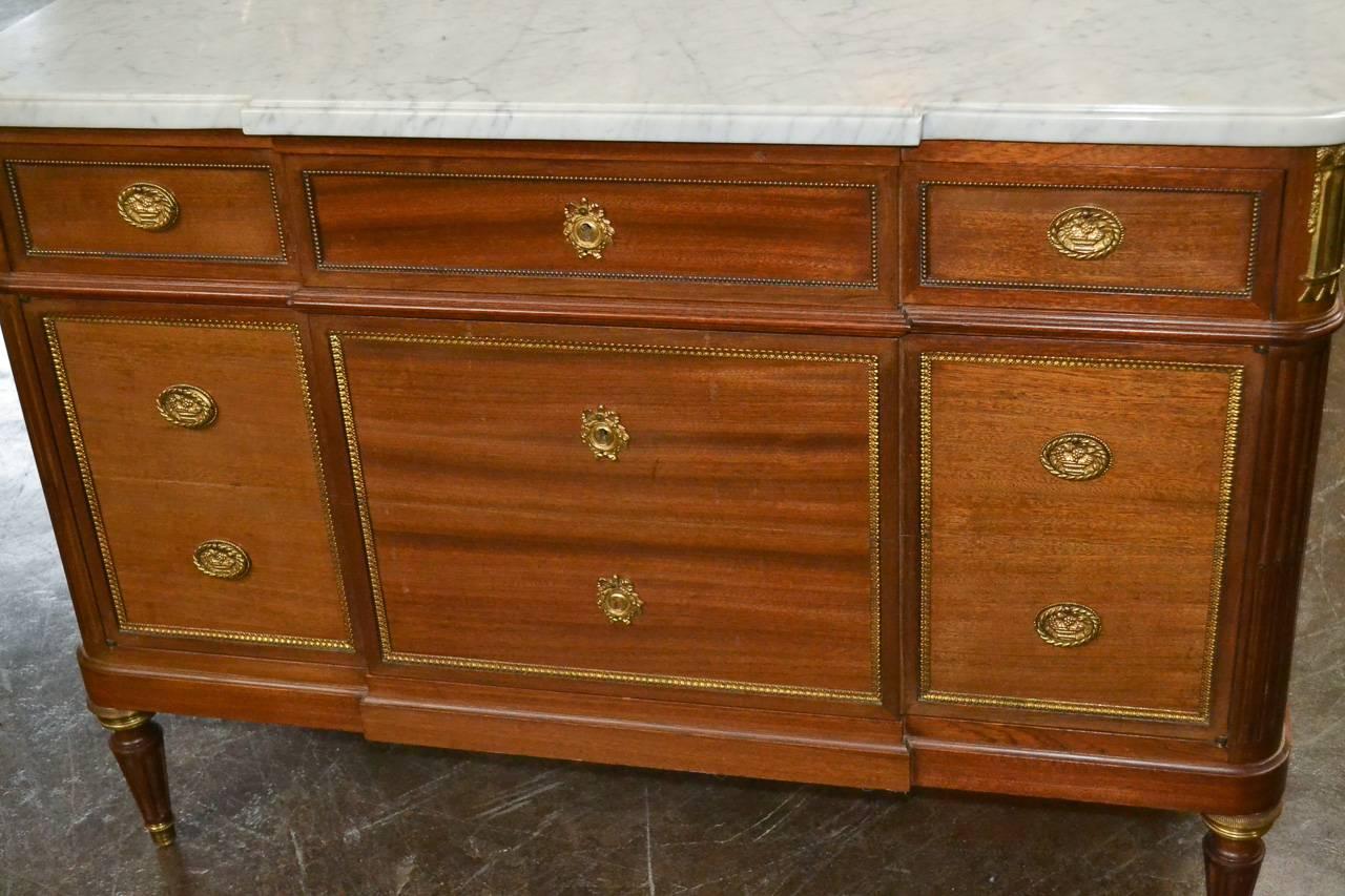 Nice quality French, Louis XVI mahogany commode. Having lovely gilt bronze hardware and trim, Carrara marble top, unusual one-drawer over three-door design, and resting on fluted tapered legs. Showcasing a gorgeous patina and straight lines great