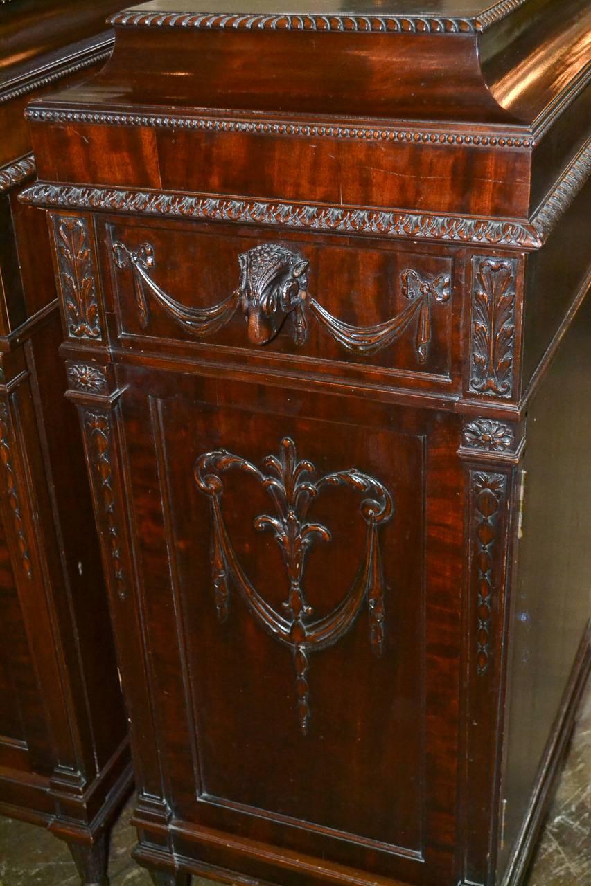 Wonderful pair of English Adams pedestal, carved mahogany side cabinets. Having lovely carved details in rams head and swag motifs, each with one drawer over one door, and possessing a rich aged patina. Great for numerous designs!