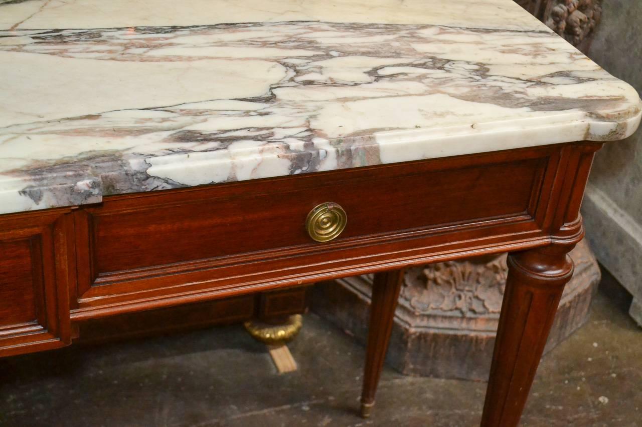 Sensational French Louis XVI mahogany three-drawer console. Having gilt bronze hardware, beautiful thick Arabscato marble top, and resting on fluted tapered legs. Exhibiting clean lines that suit many decorative styles!