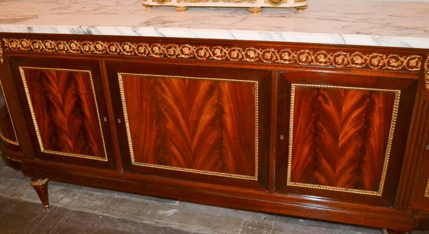 Exceptional French gilt bronze mounted mahogany four-door sideboard. Having lovely gilt bronze mounts in acanthus leaf motif, impressive Arabscato marble top, a rich warm patina, and resting on tapered legs. A sophisticated piece with classic lines