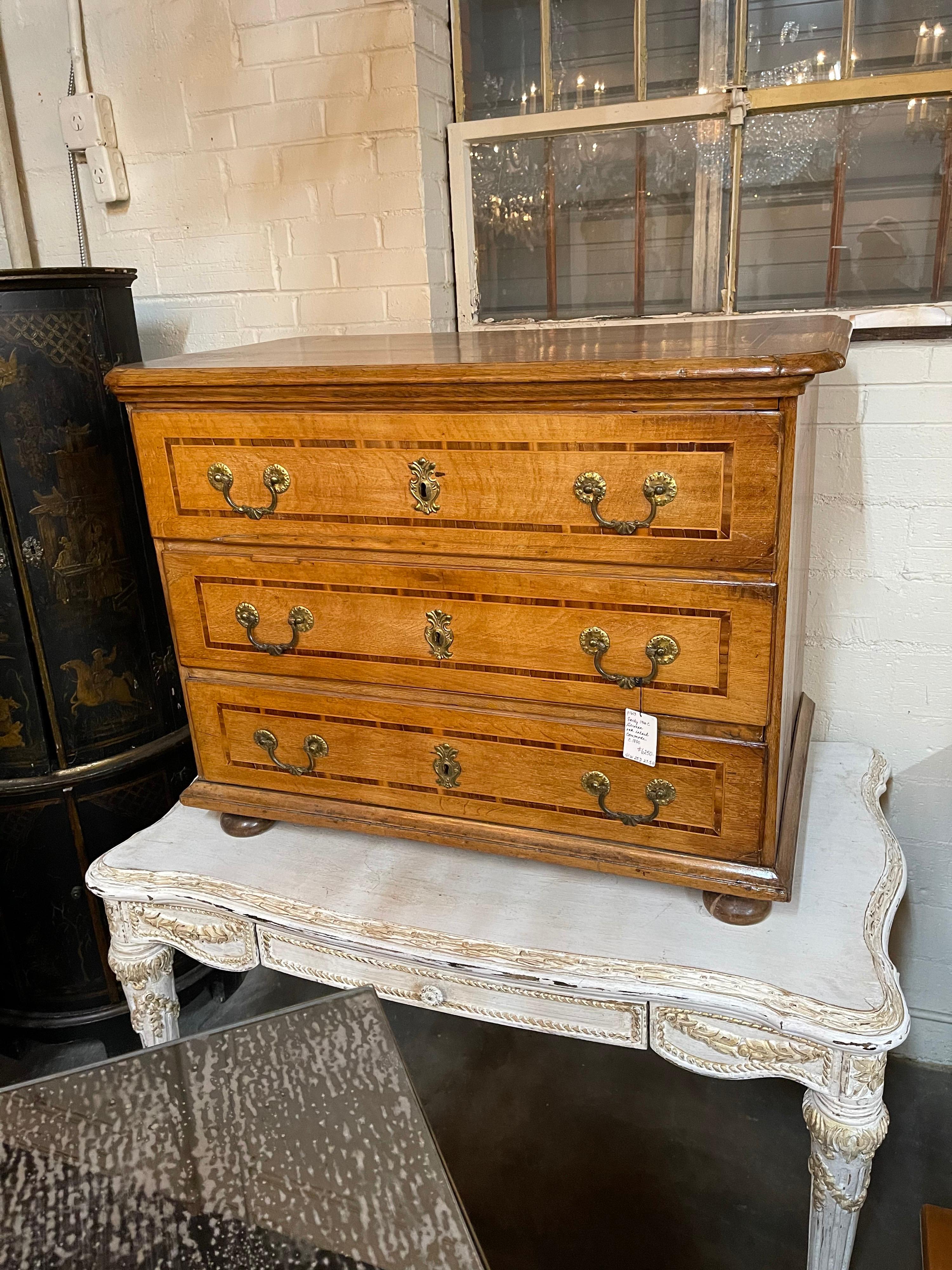 Understated 19th century German tiger oak and rosewood banded commode with inlaid top. The three drawers with tastefully appointed brass pulls and escutcheons. 

The entire raised on carved bun feet.

Superb slightly faded patina,

circa 1840.