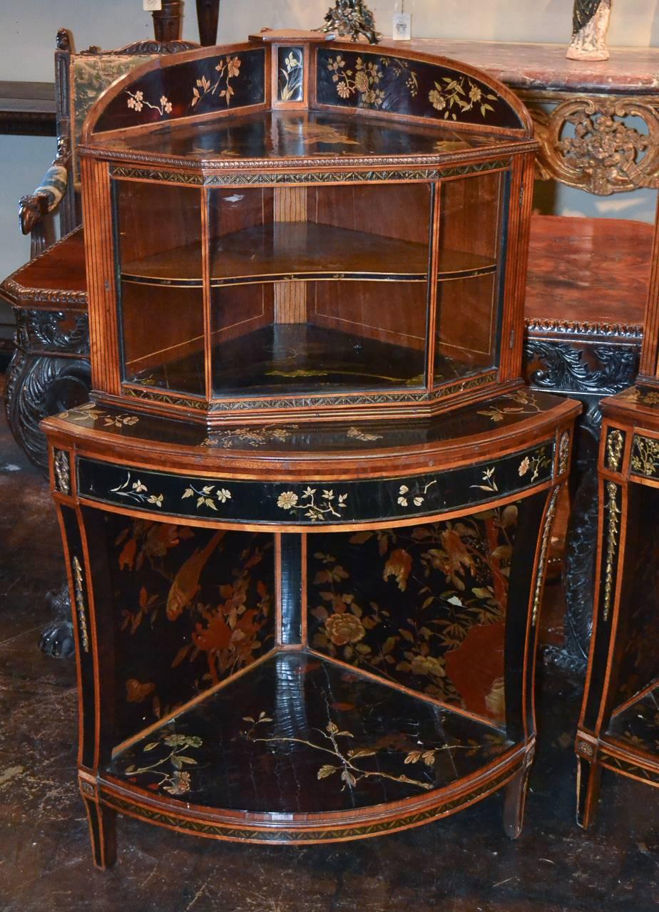Extraordinary pair of English Chinoiserie decorated corner cabinets circa 1880.  Having shaped fronts with vitrine tops enclosed by 3-panel glass doors, adorned in oriental floral and landscape motif, and with lovely black lacquered finish. 