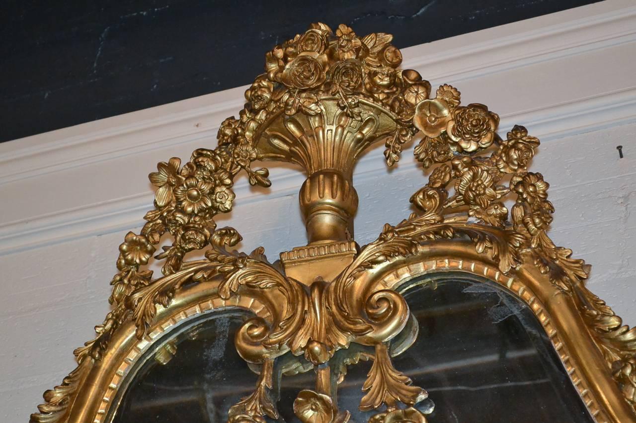 Sensational large French, Louis XVI giltwood mirror with original beveled glass. Having elaborately hand carved cartouche in floral motif, and with acanthus leaf accents along frame. The mirrored glass in the side panels are beveled as well as the