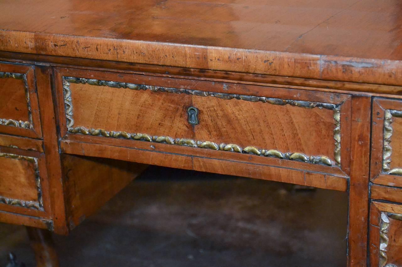 Delightful 19th century English neoclassical walnut 5-drawer writing desk, circa 1860. Having gilt gesso trim, shaped trestle legs terminating in claw feet, and wonderful rich warm patina.