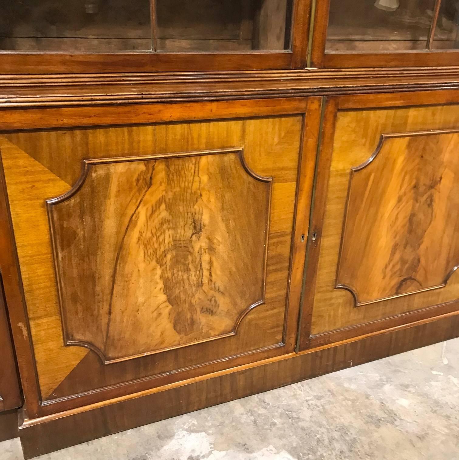 Very fine quality 18th century George I English figured mahogany breakfront bookcase with reeded trim. 

The simplistic cornice sits atop large original glaze paned doors with Gothic influenced astragal mouldings and a lower section with four