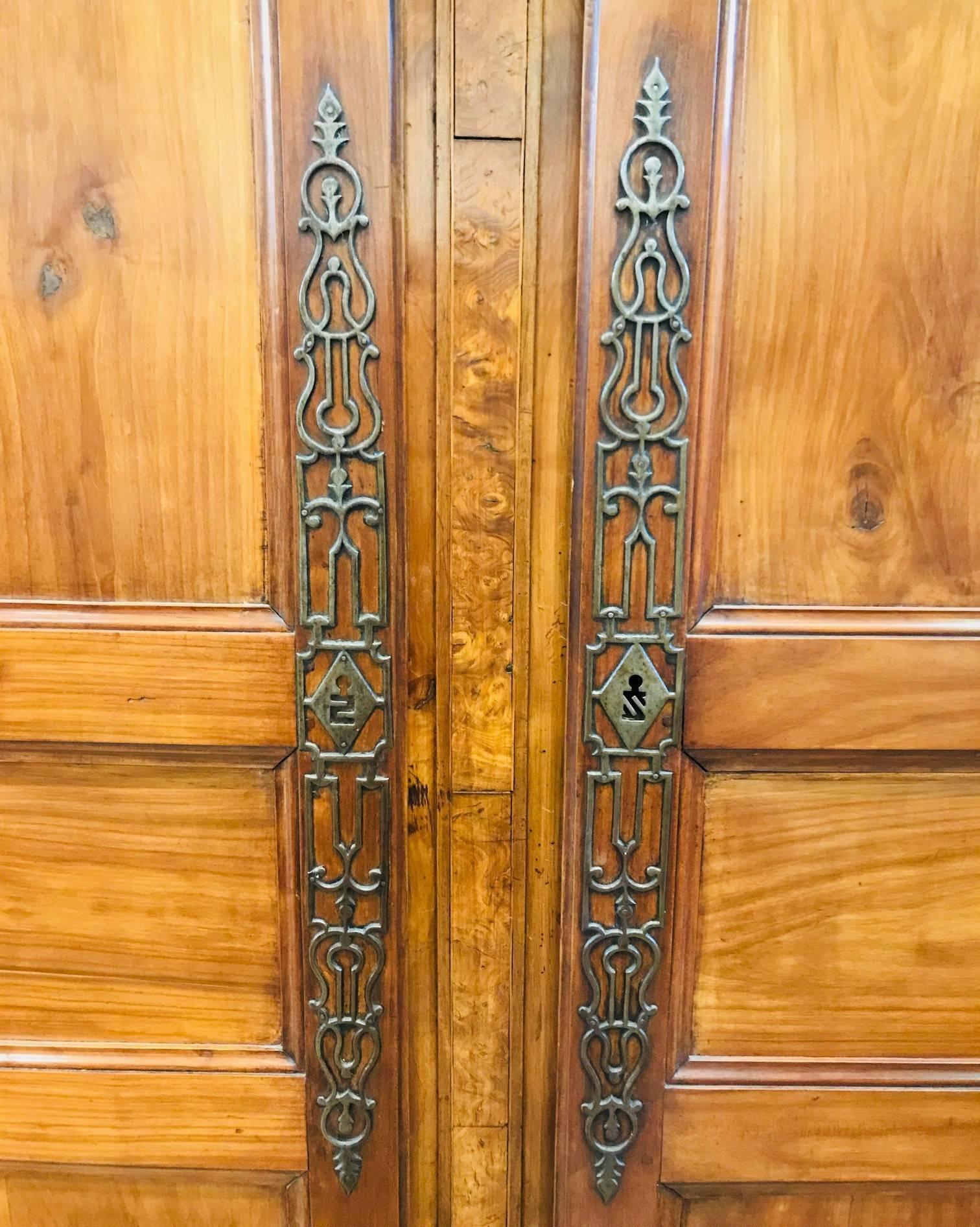 Particularly fine 19th century, French cherrywood armoire or wardrobe from Saintonge.

The serpentine-shaped and marquetry inlaid bonnet above two doors with hand-wrought filigree escutcheons separated by a thin strip of burled wood. 

The skirt