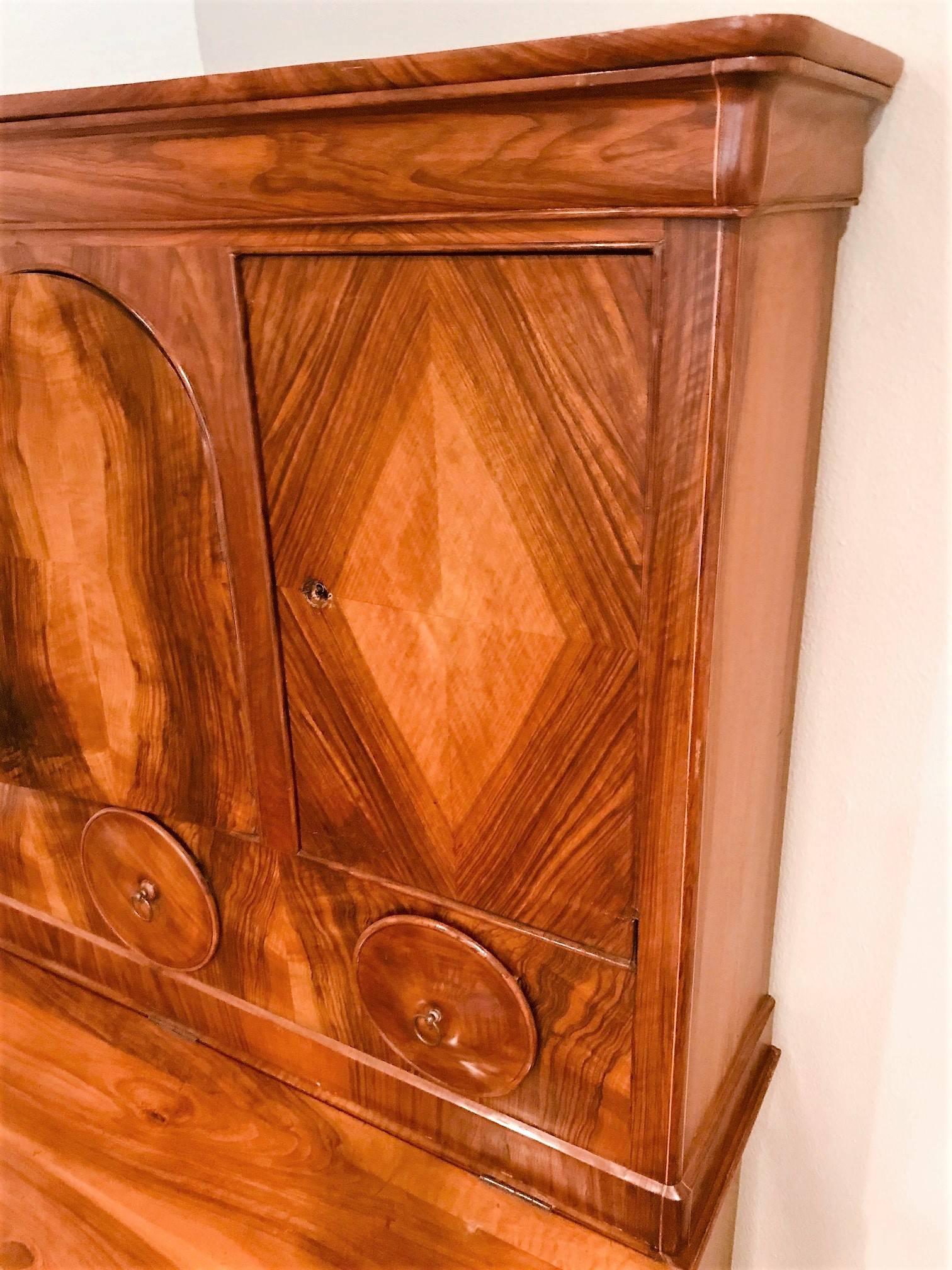 Outstanding antique Northern European Biedermeier style bureau bookcase in exotic veneers.

The top section with a lift top for secret storage above cabinets and three drawers with unique circular facings. The lower portion with a contoured