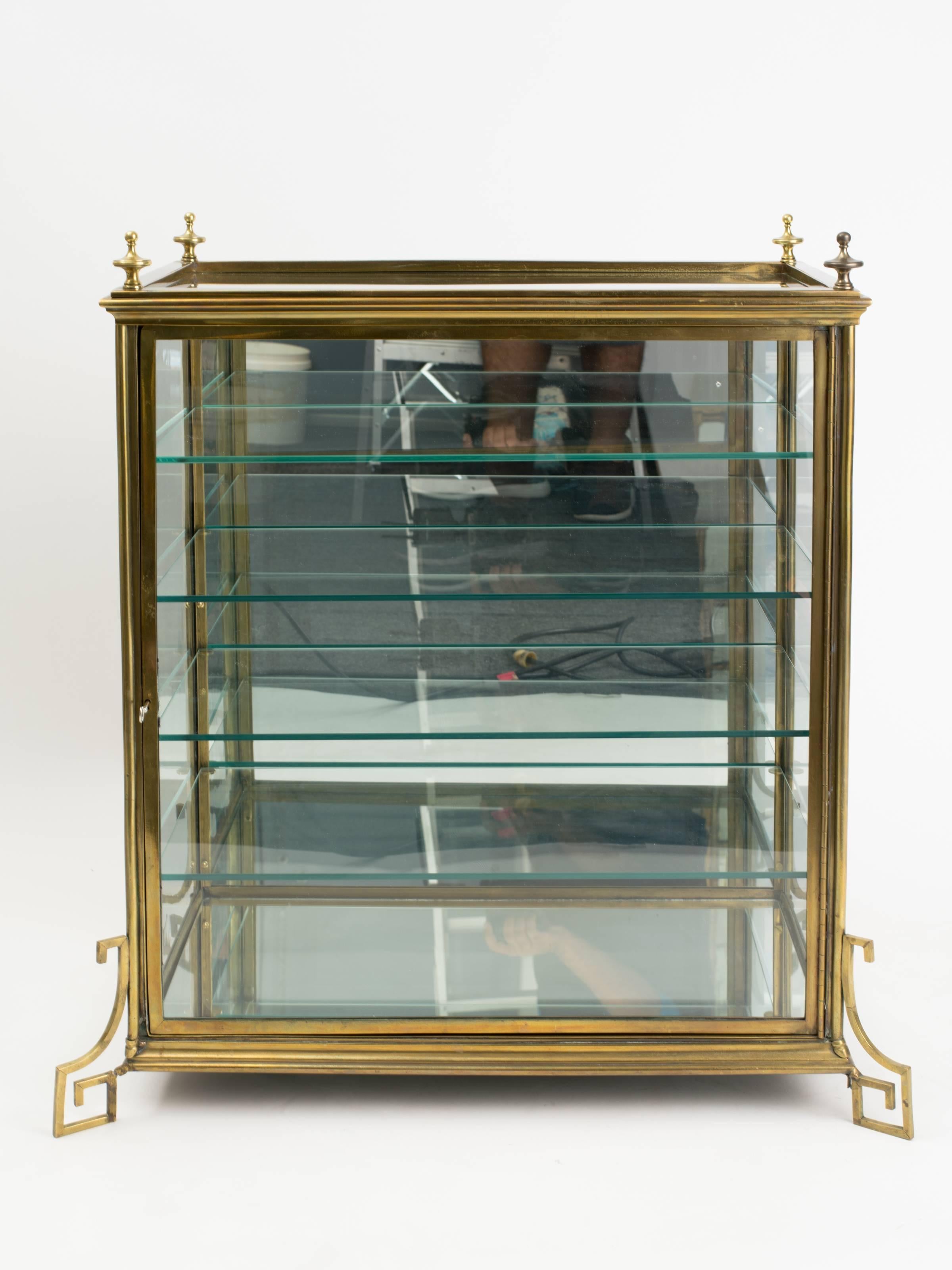 A midcentury brass curio cabinet featuring Greek key legs and mirror backing.
Original lock and key.