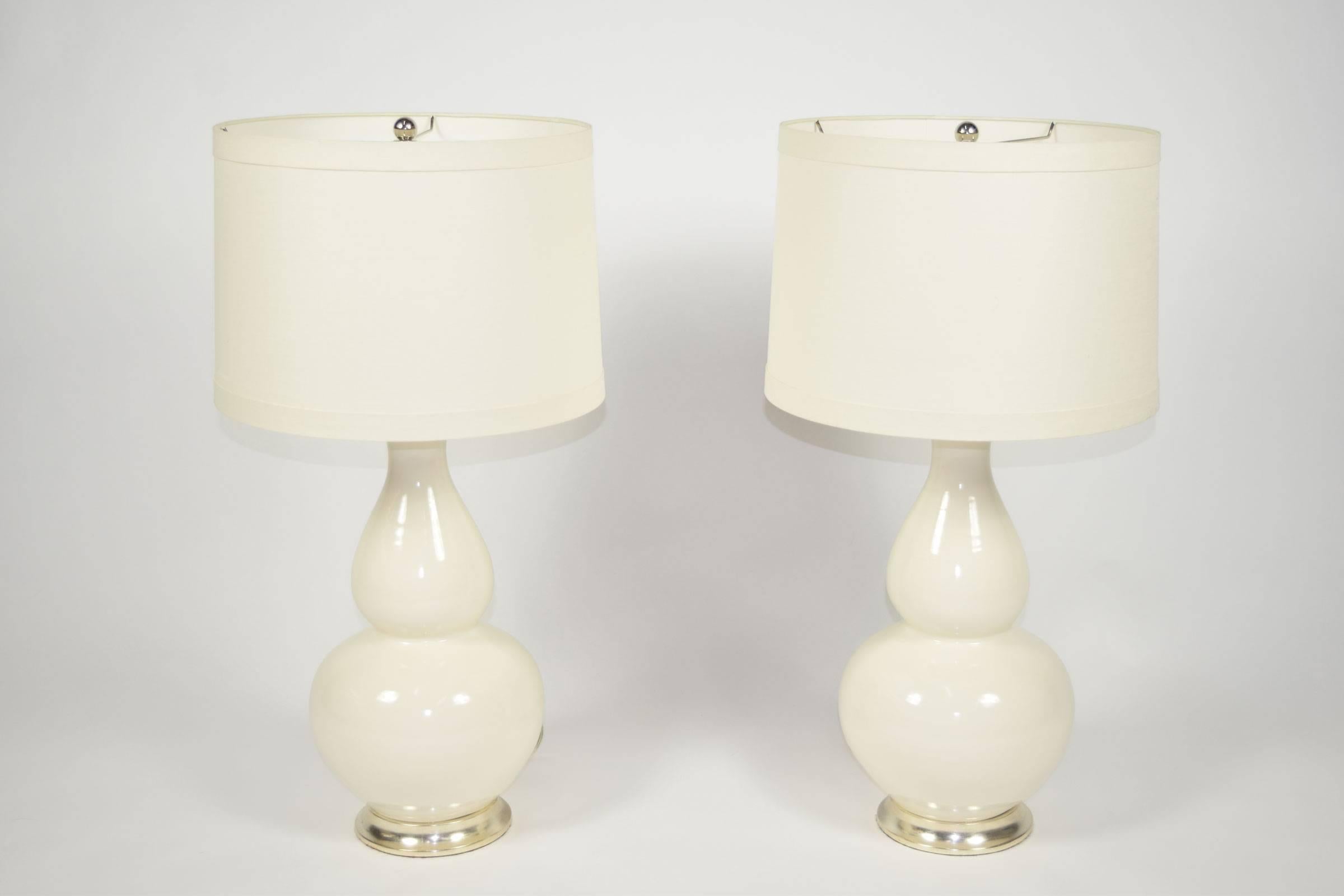 A gorgeous pair of Christopher Spitzmiller lamps in white ceramic with silver leaf bases and chrome lighting fixture. Shades are included and are a white linen with banding on top and bottom. Height is adjustable on these lams. The measurements