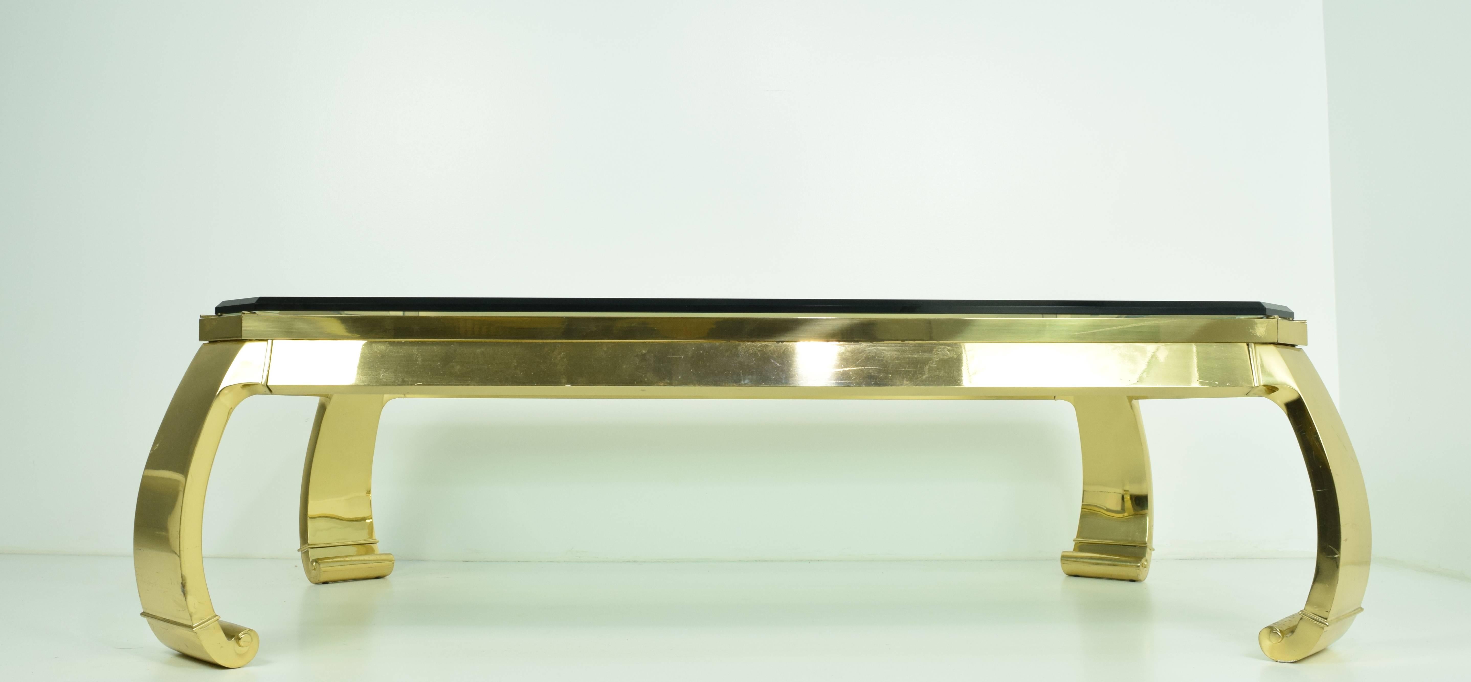 A large 1970s solid brass coffee table in the style of designer Karl Springer. The table features a thick 3/4 inch chamfered glass top with cut corners and Ming style curved legs. .Heavy brass base with thick glass top, made in Italy. 