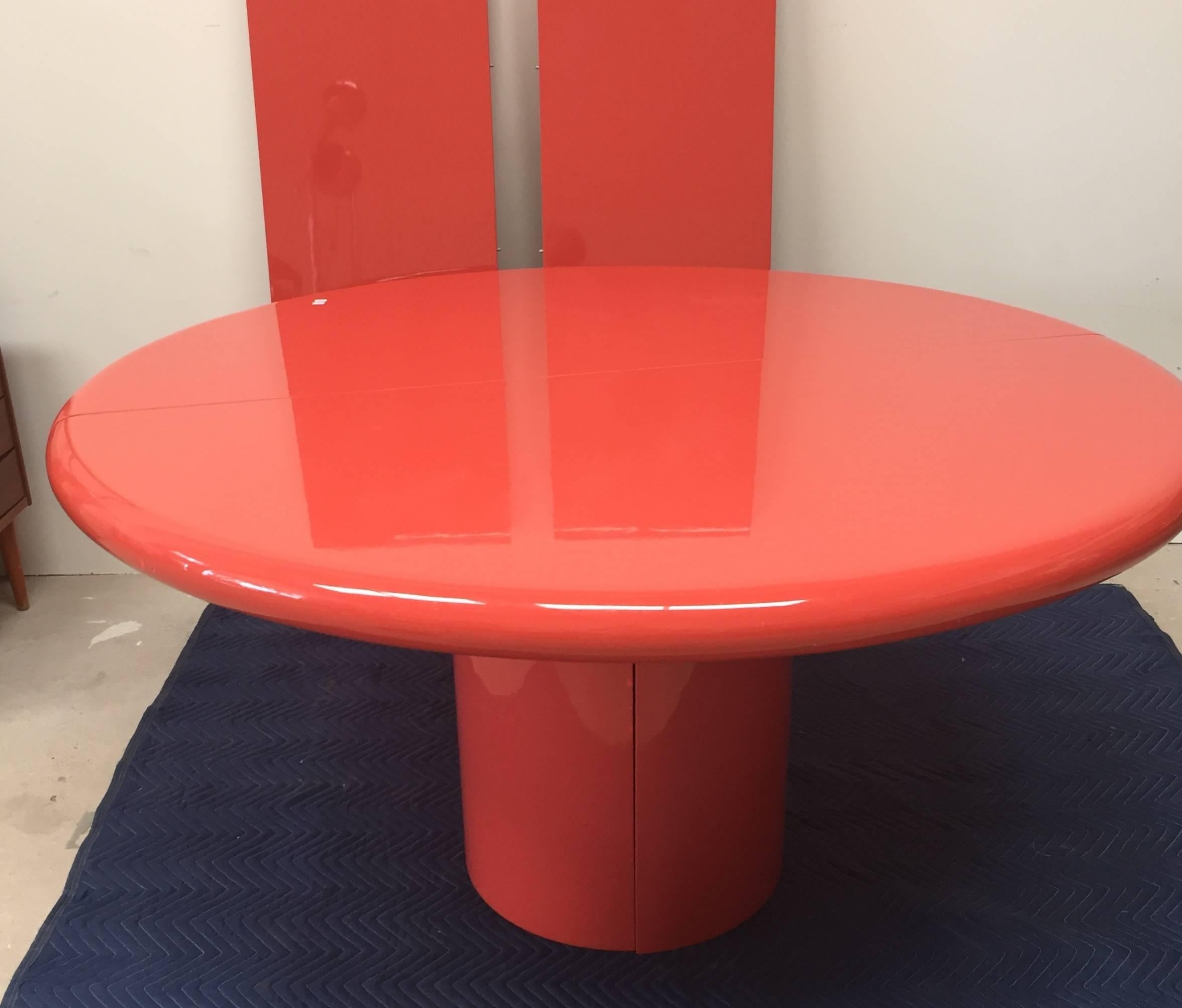 The vibrant coral color of this iconic table adds a playful and sophisticated note to a dining area. The top, with its bullnose edge, rests on a round cylinder base. 
The two leaves are each 18