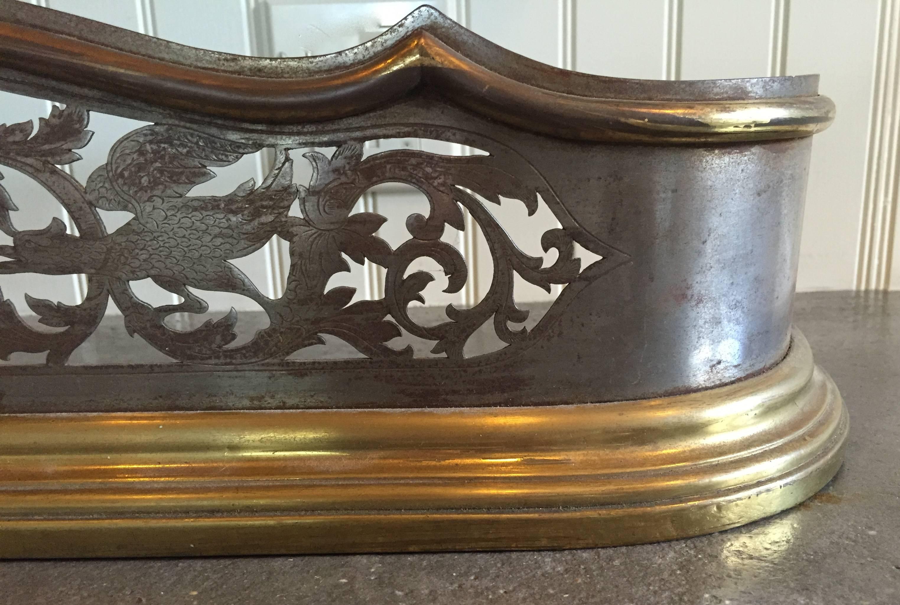 Finely detailed with a hand pierced and incised design showing fanciful birds, dragons and flora, this fireplace fender is steel, surrounded by upper and lower molded edges of polished brass.

It is left as is with its wonderful patina of age, but