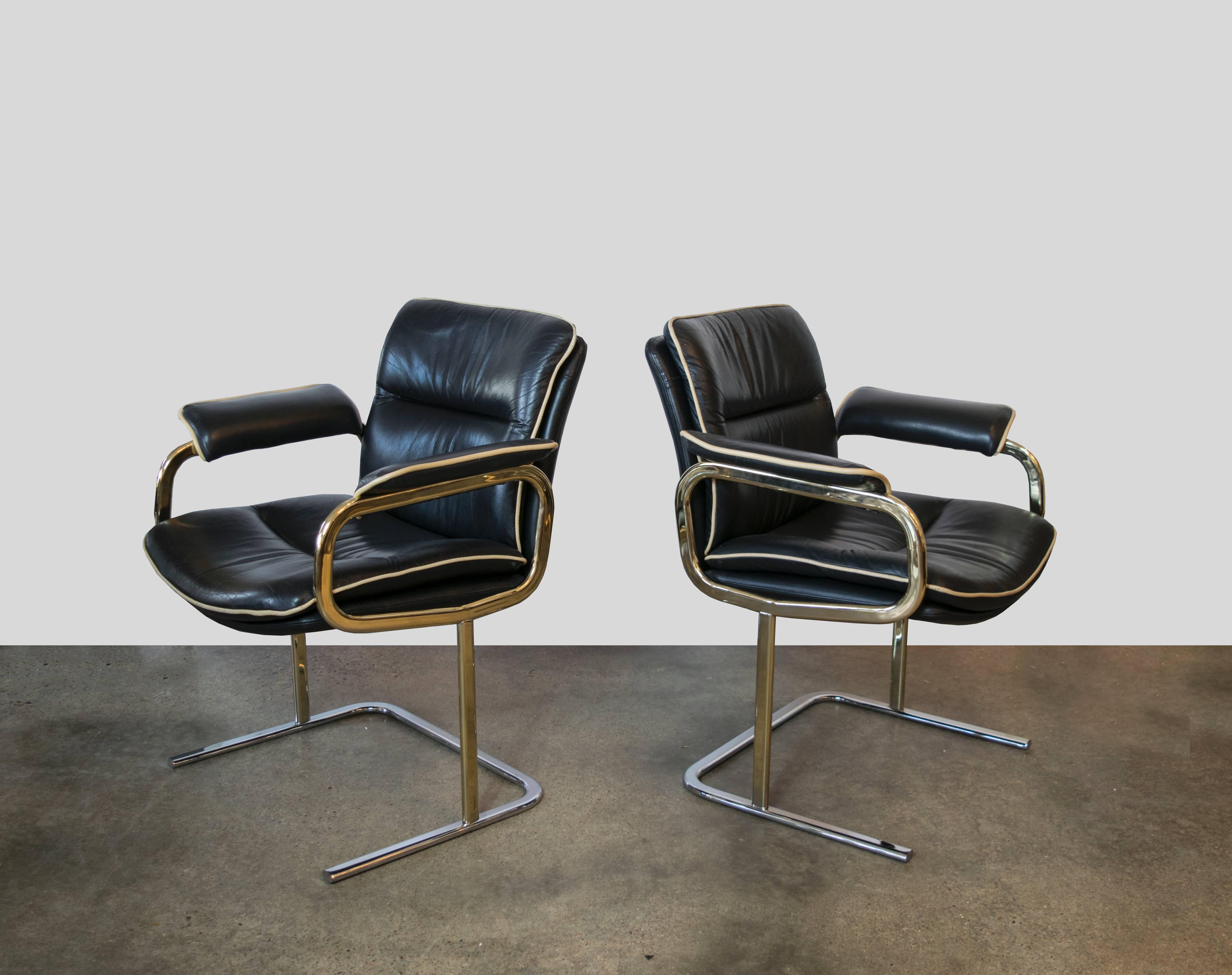 This black leather chair with matching ivory leather piping is highly unusual in its design. The rounded looped arms are topped with padded armrests and the brass chair is complemented by a chrome base. One available only.