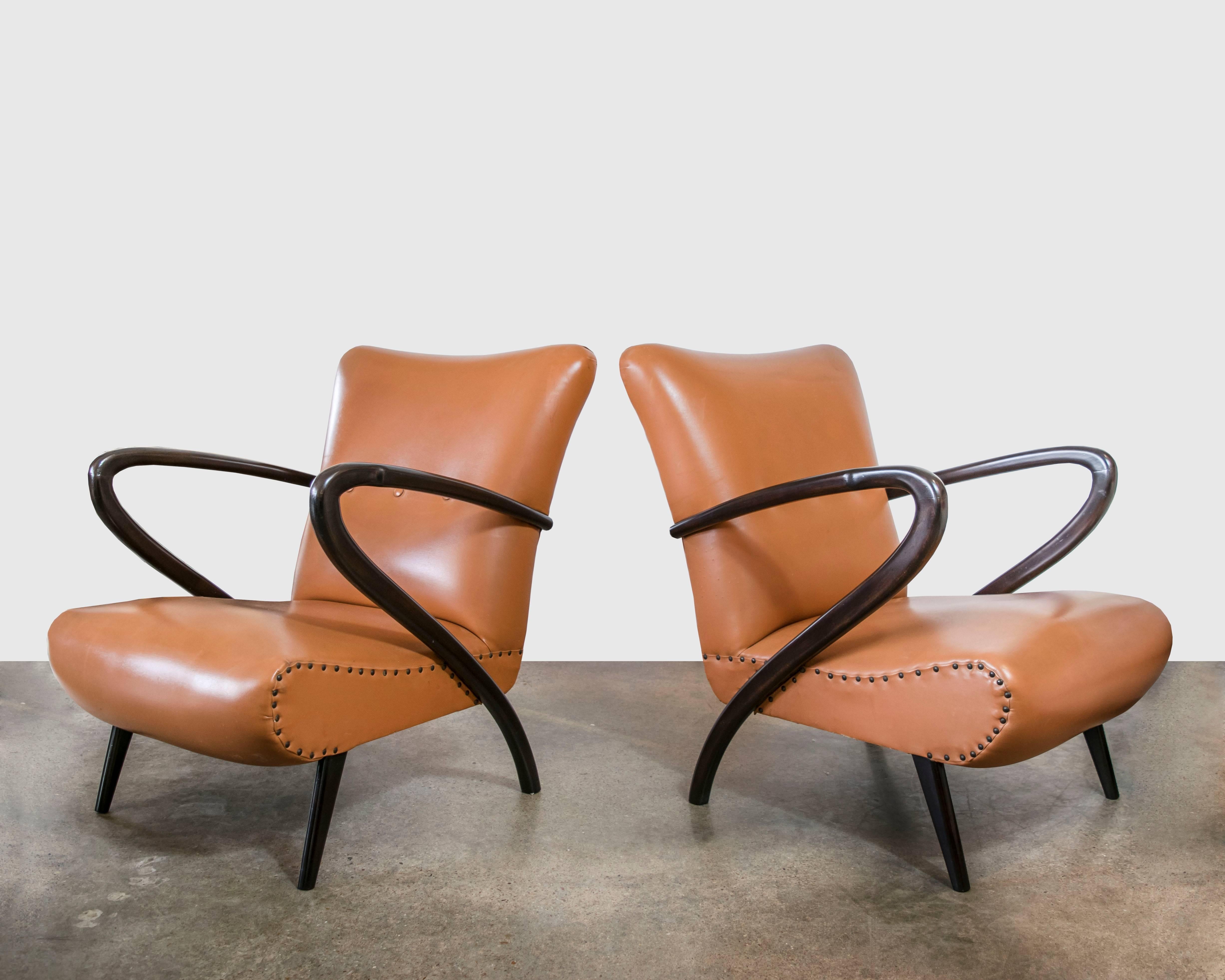These chairs are still in their original pleather from the 1950s and need to be recovered but the style of this chair is so unusual with a mahogany combination arm and leg with the arm rails curving down and becoming the back leg.