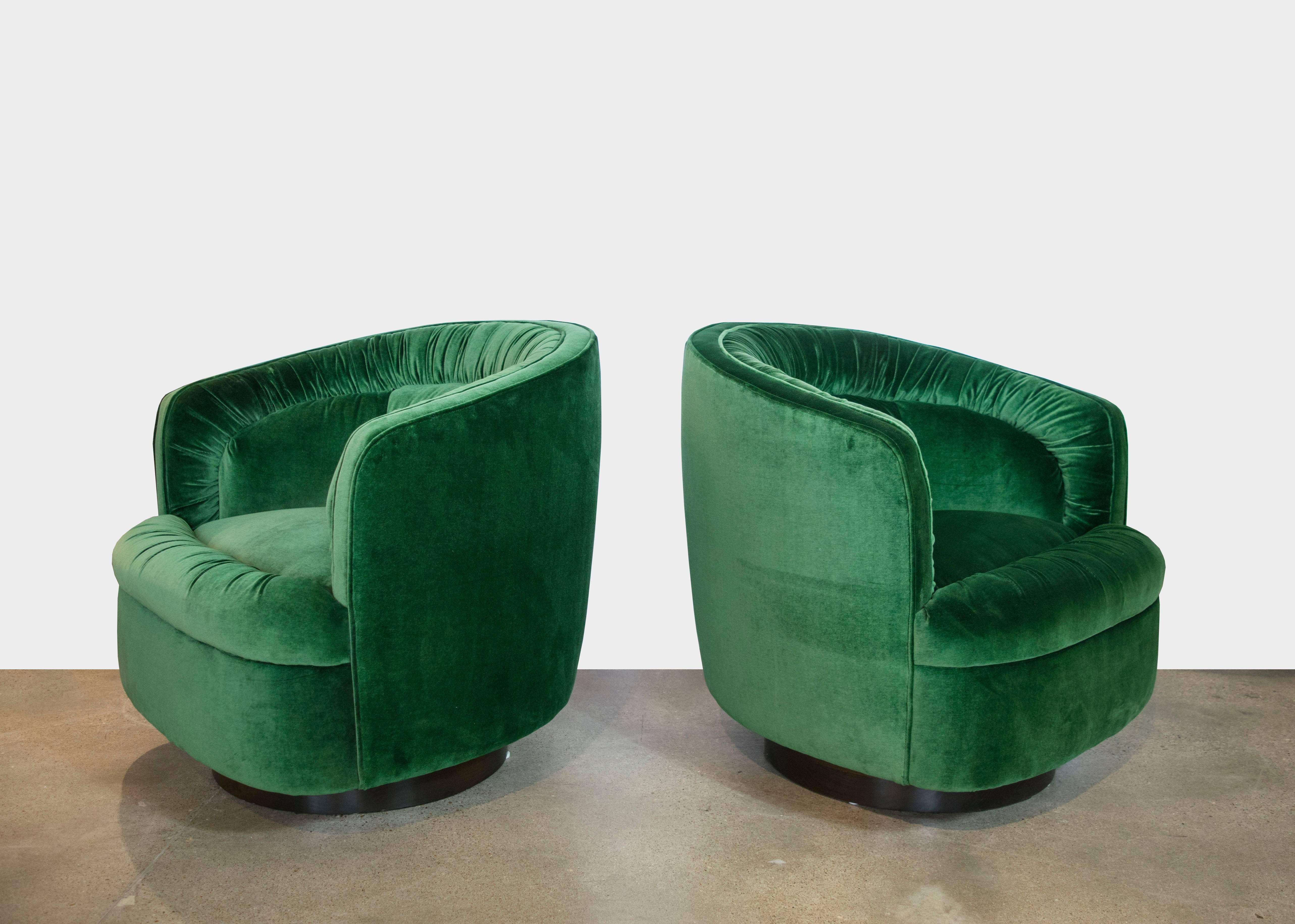 Extremely plush and elegant emerald green velvet swivel chairs with dark brown wooden bases. The chairs have ruched tufting and they swivel a full 360 degrees.