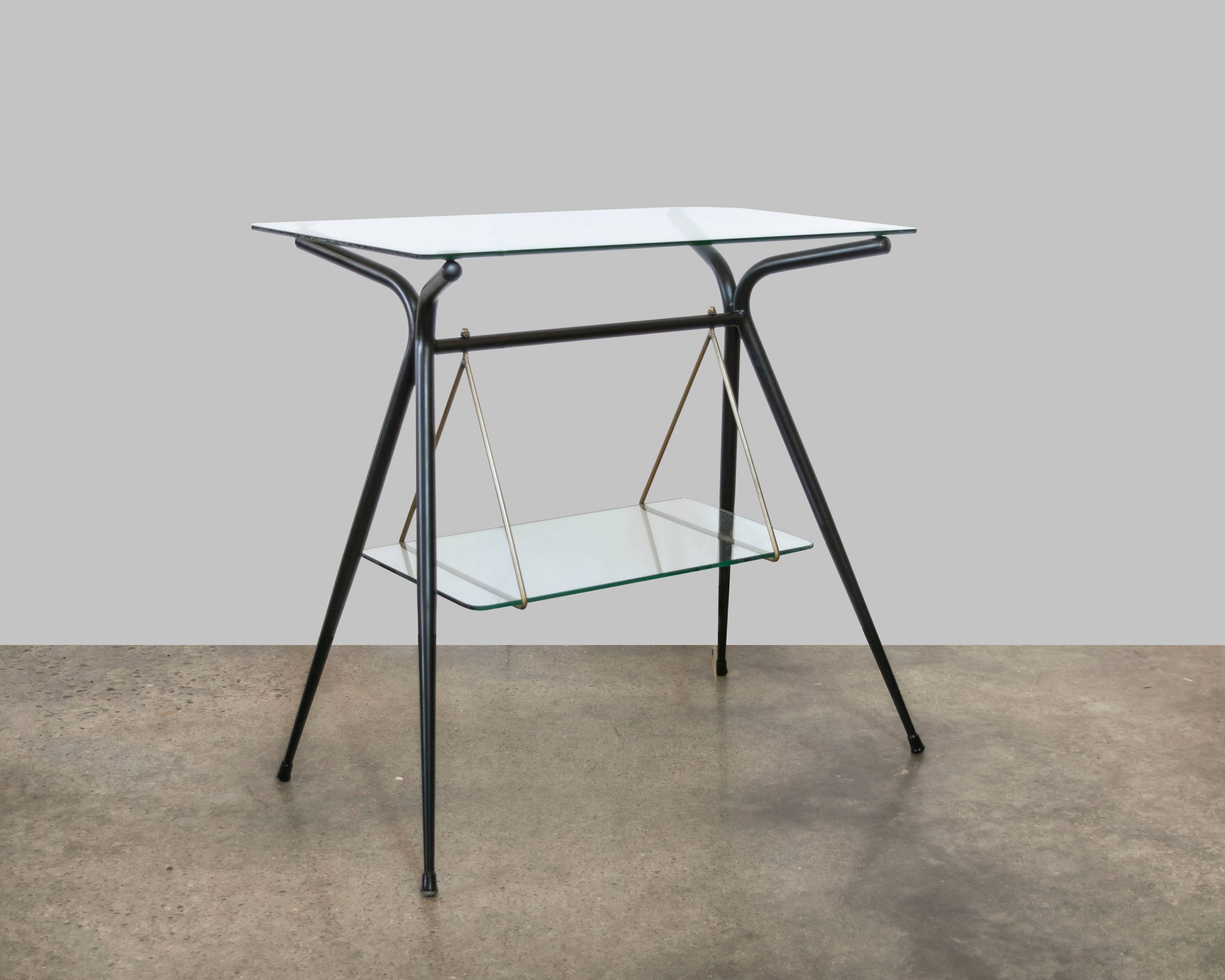 A beautifully designed two-tier glass, brass and black lacquer table with an interesting triangular brass bracket which holds the bottom shelf, with beautifully sculptured black lacquer double sided legs.