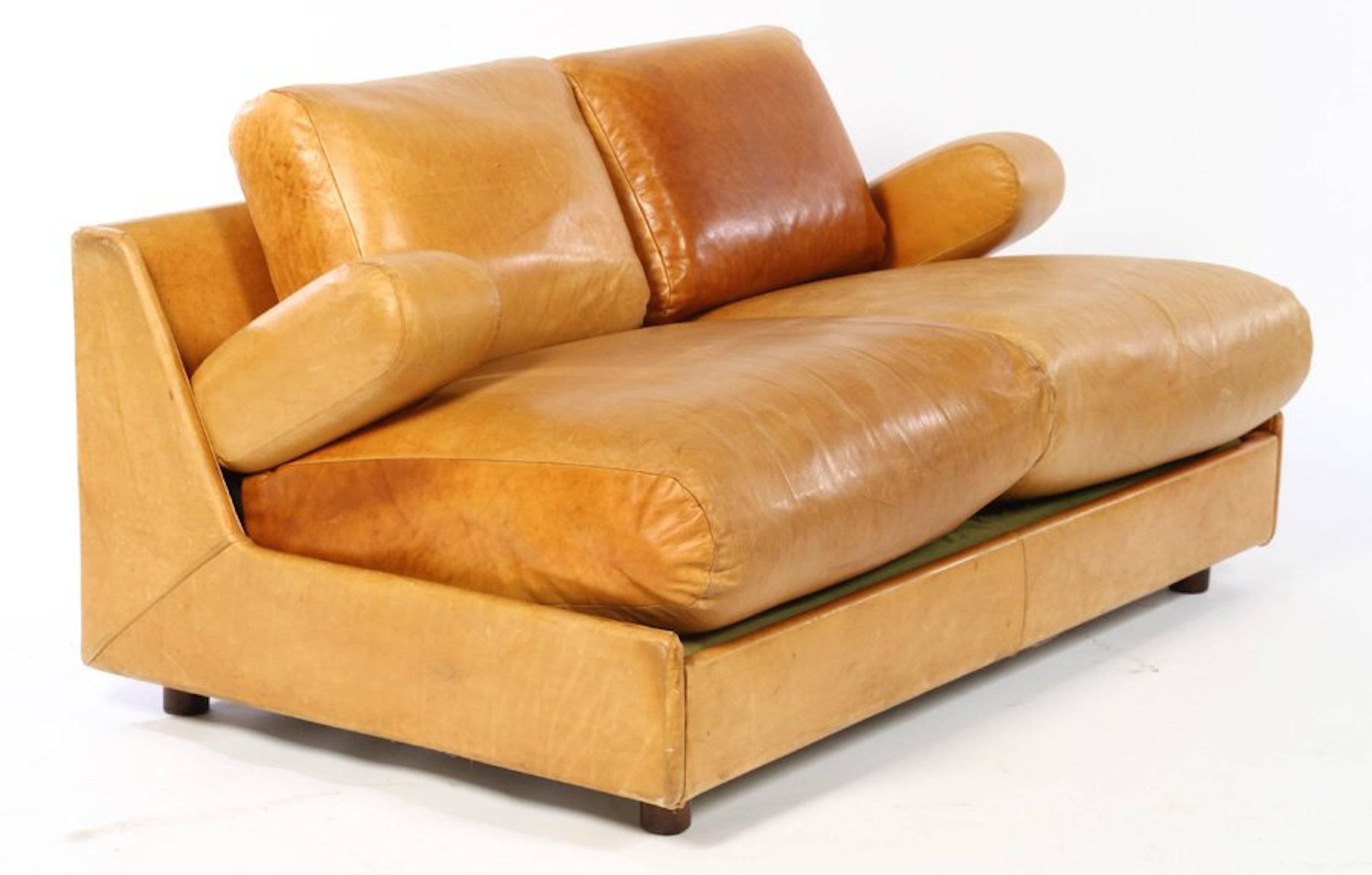 A Mid-Century Modern leather sofa having four loose cushions and articulated armrests, all raised on cylindrical feet, Italy, 1970.

Dimensions: Seat height 18.5