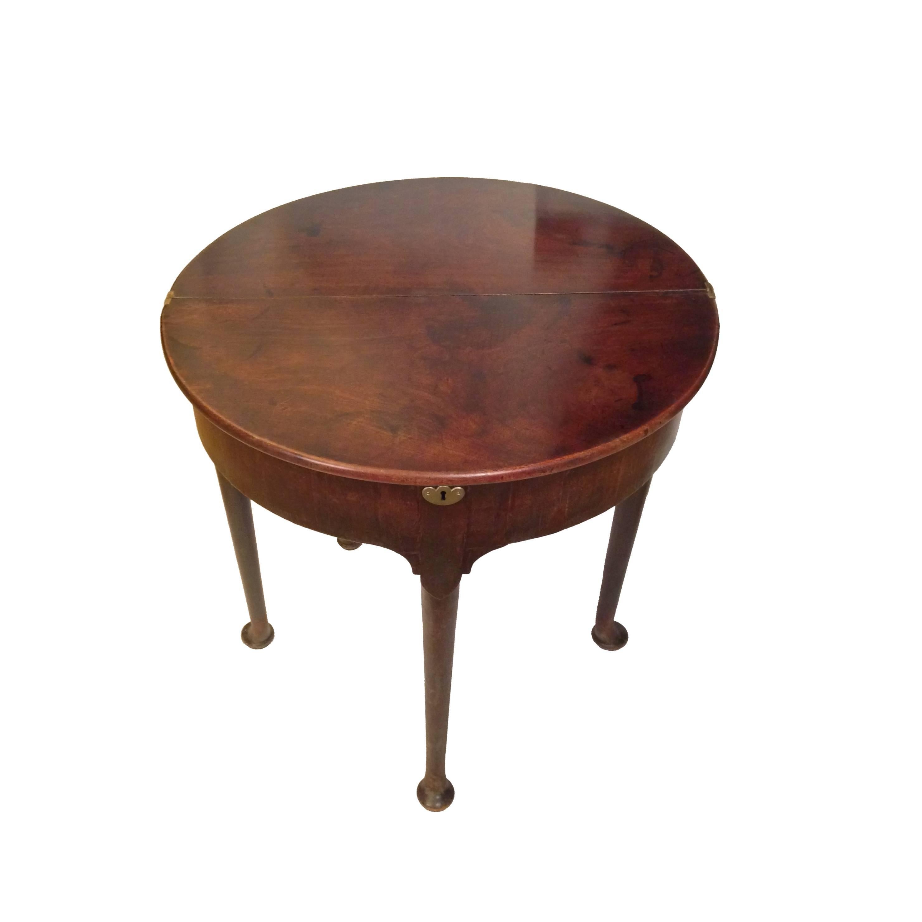 An 18th century mahogany demilune tea table with fold over top enclosing a storage well. The double hinged tabletop lifts and folds back, supported by a single gate leg, which creates a circular surface area. Turned, tapered legs with pad